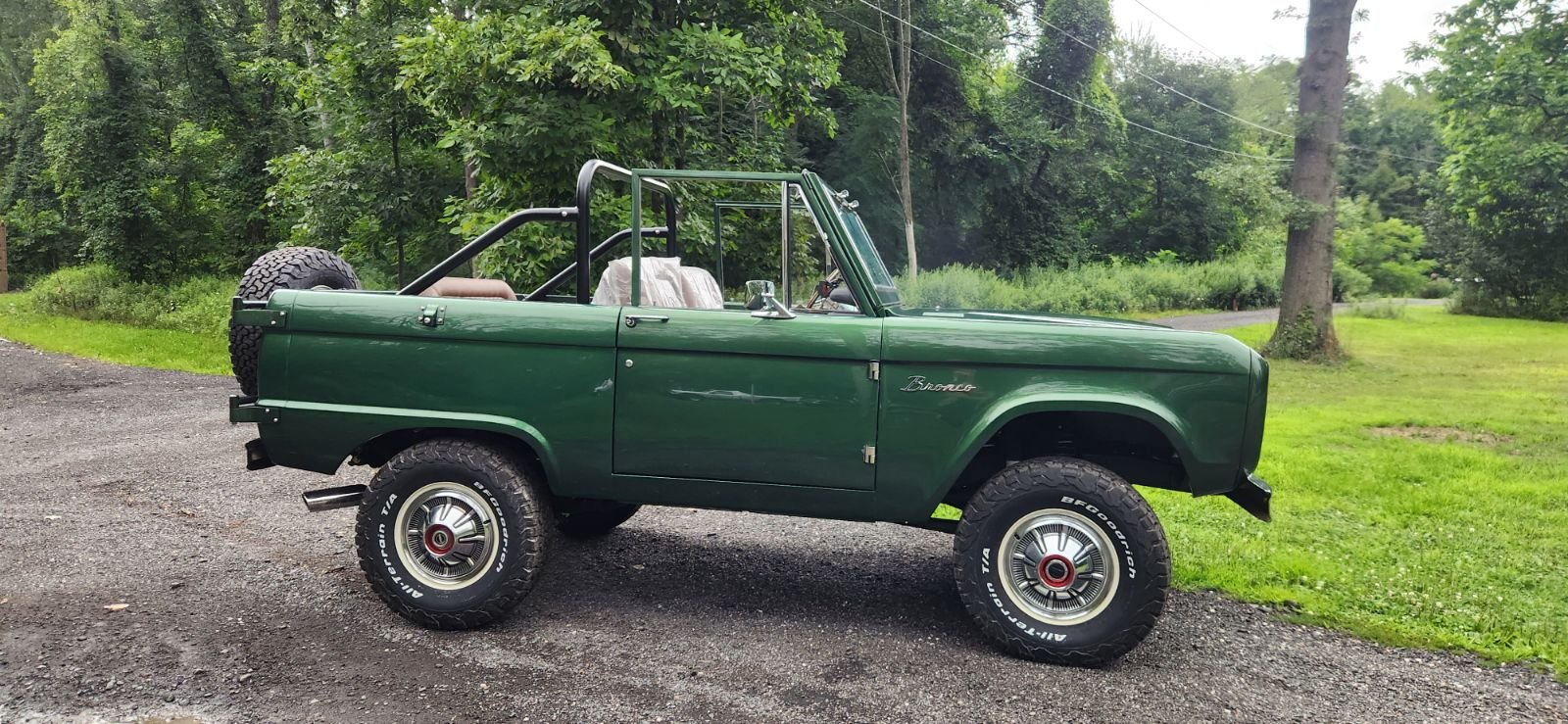 Green vintage off-road vehicle parked on a gravel surface with a grassy background and trees.