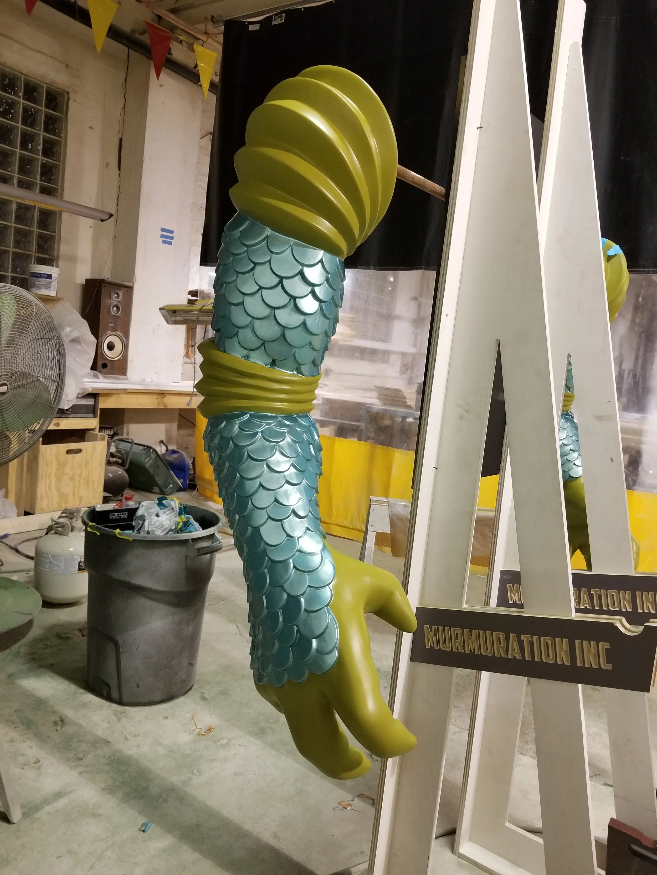 A colorful sculpture reptilian arm with green fins and blue-green scales located in an artist's studio.