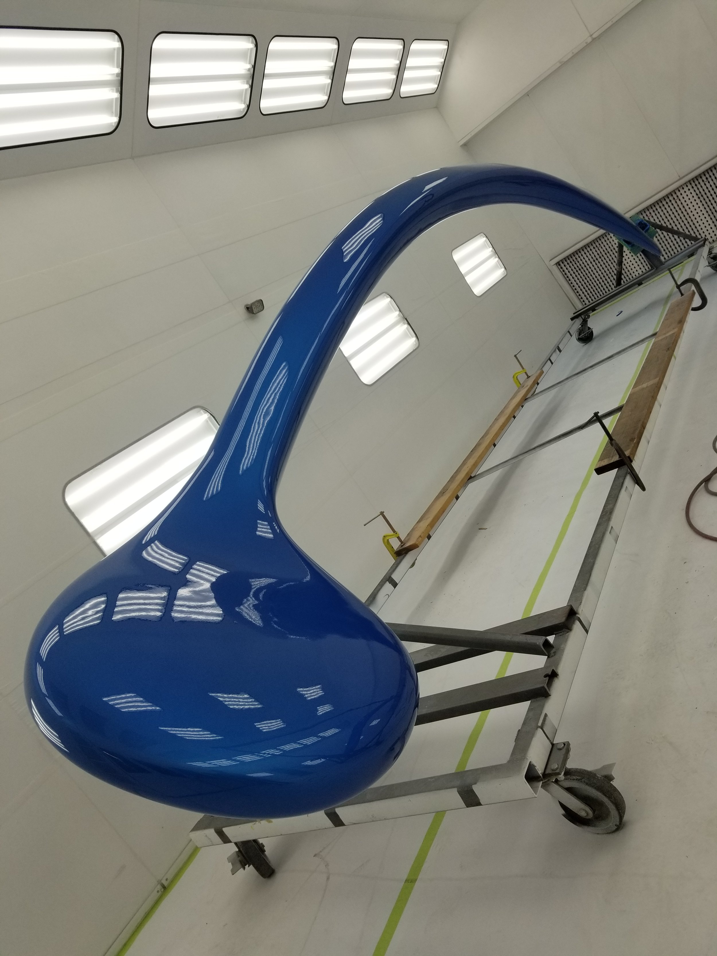 A large, shiny, blue sculpture resembling a musical note on a metal stand with wheels inside a well-lit, white room.