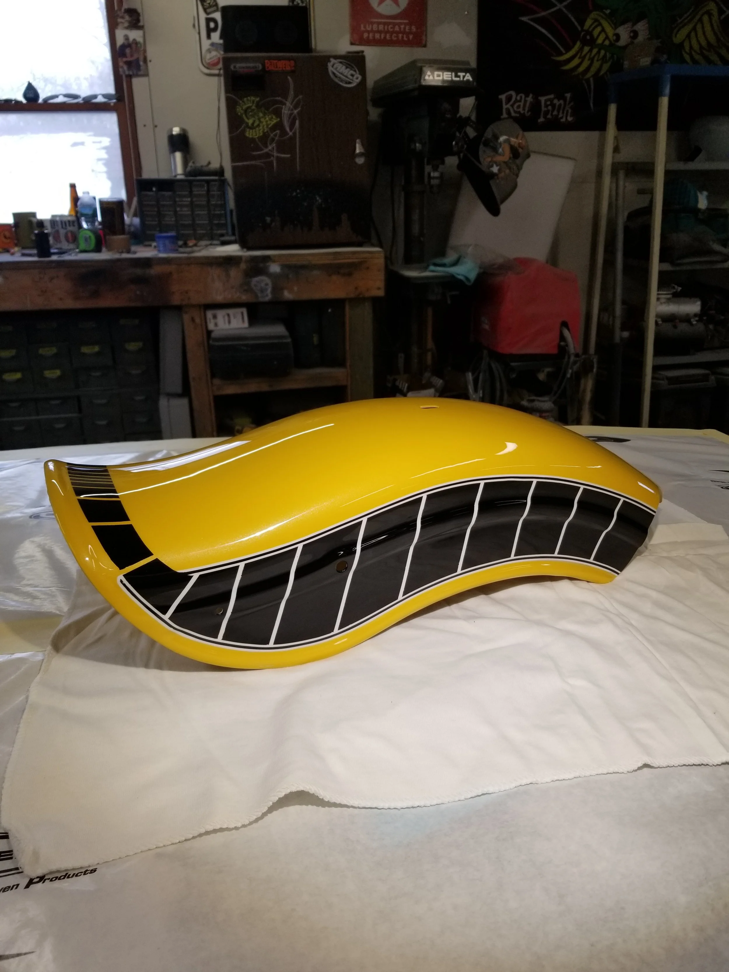 A yellow and black custom painted motorcycle part resting on a white cloth in a workshop.