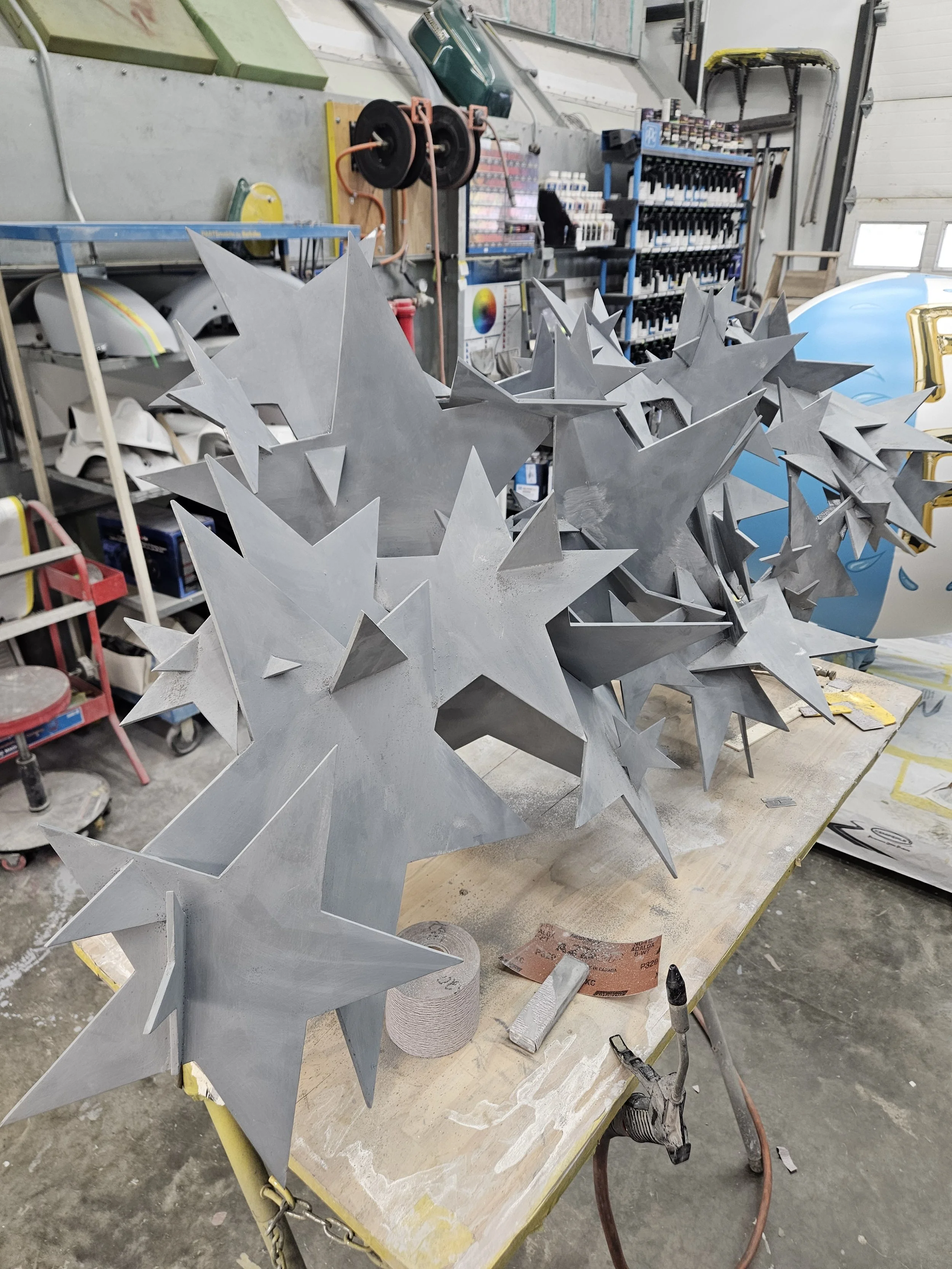 Multiple large, metallic five-pointed stars with sharp edges arranged on a worktable in a workshop.