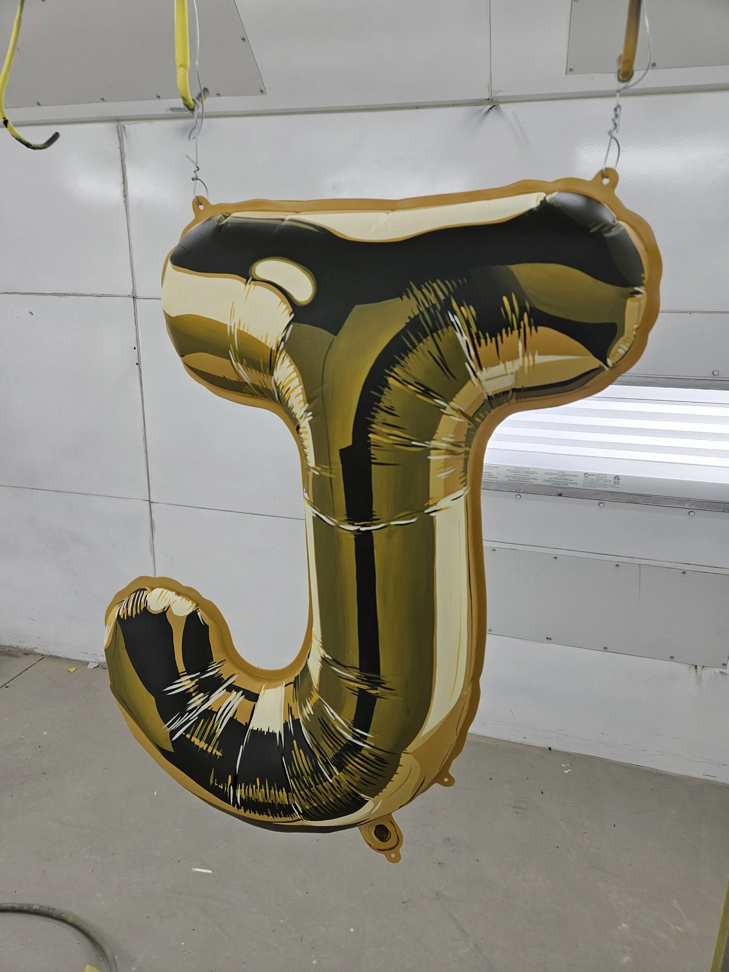A large, gold and black number 1-shaped balloon hanging in a room with white walls and a gray floor.
