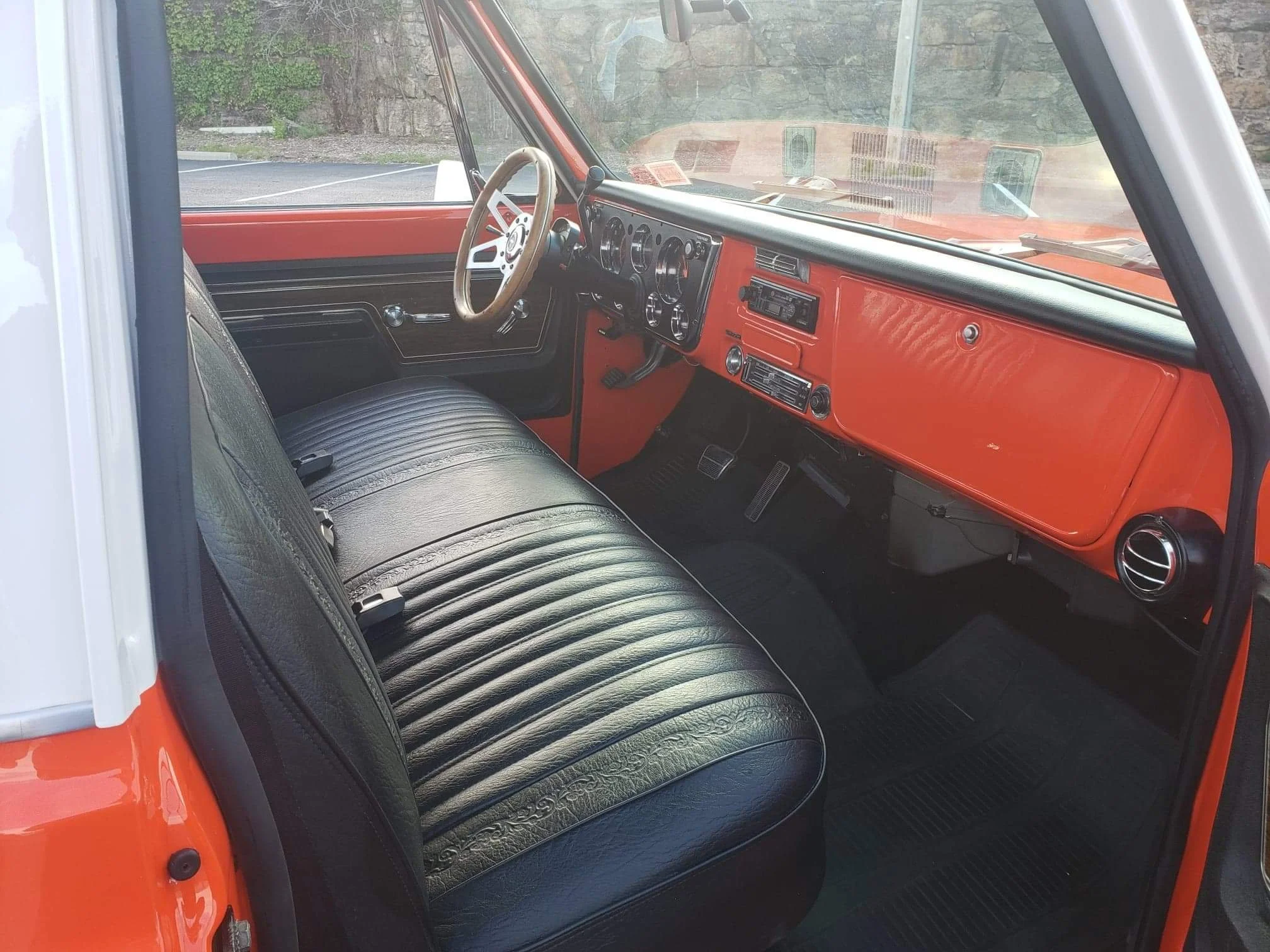 Interior of a vintage vehicle with a black steering wheel, black leather bench seat, orange dashboard, and orange door panels.