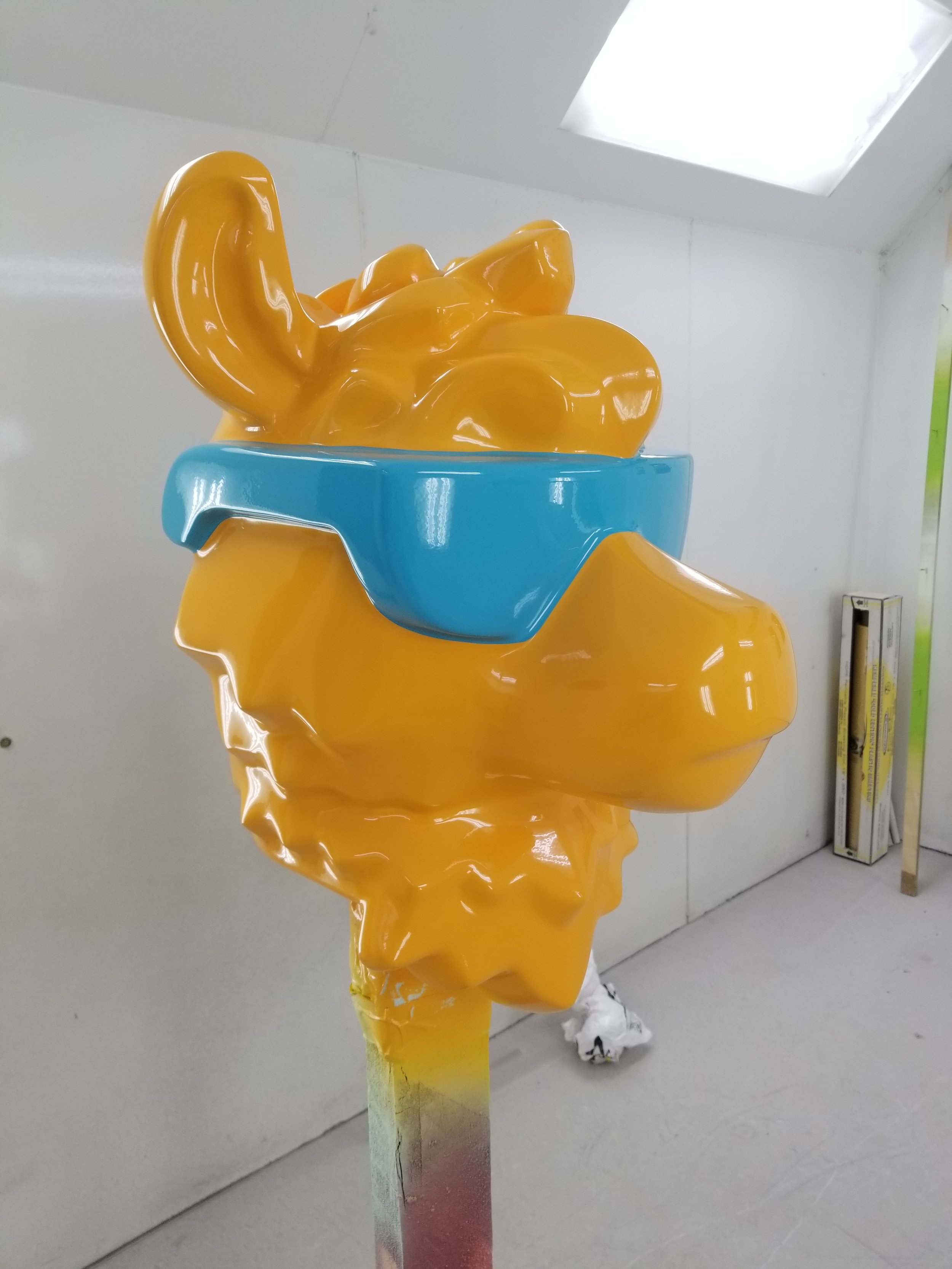 Colorful sculpture of a LEGO camel's head wearing blue sunglasses and a crown, mounted on a multicolored pedestal.
