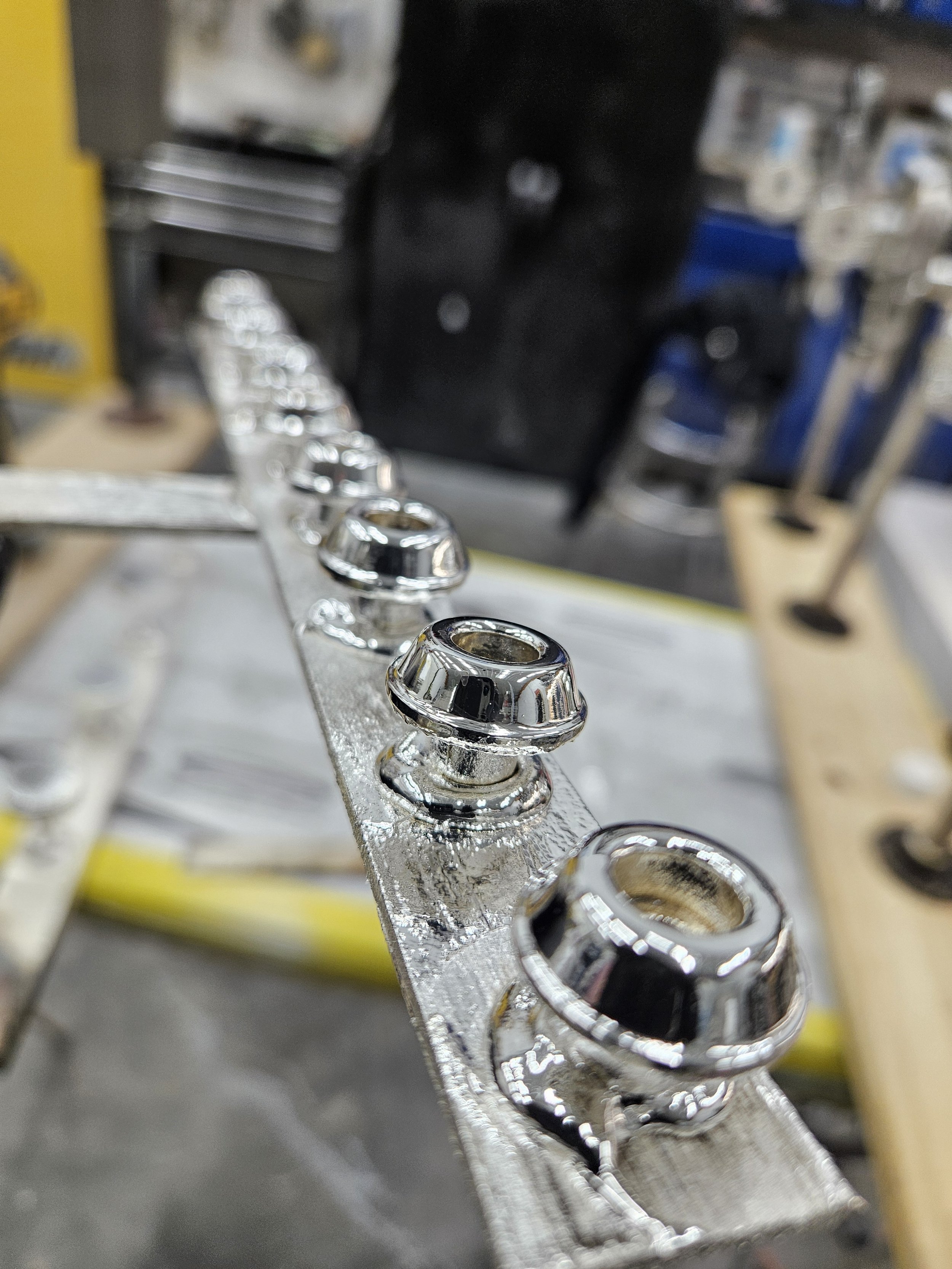 Close-up of shiny metal motorcycle parts, possibly wheel hubs or spacers, mounted on a workbench in a workshop.