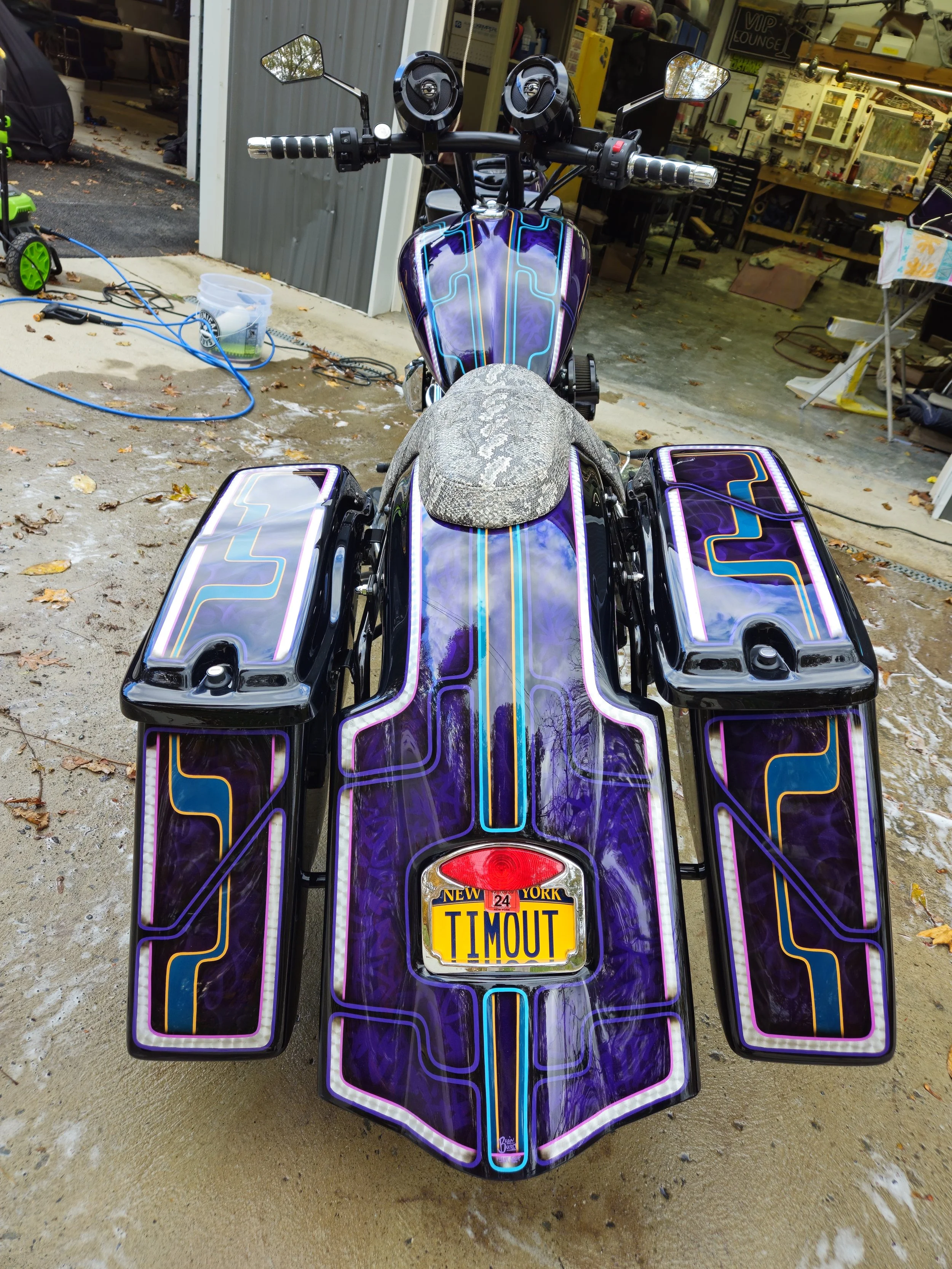 Rear view of a custom motorcycle with vibrant purple and black paint, neon-like outlines, and a 'TIMOUT' New York license plate.