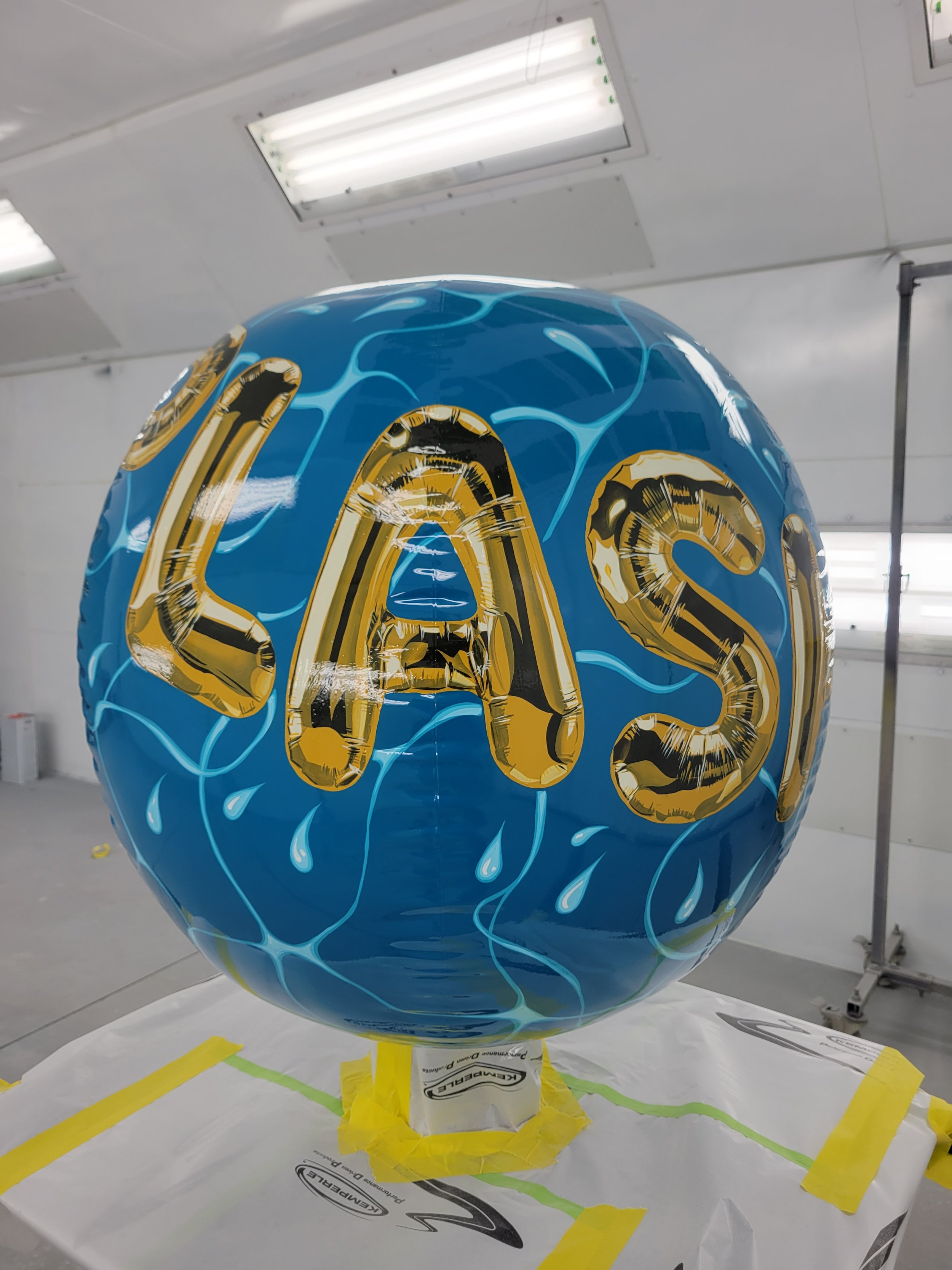A helium balloon with a blue background with large gold balloon letters, decorated with water droplets and blue lines resembling water splashes.