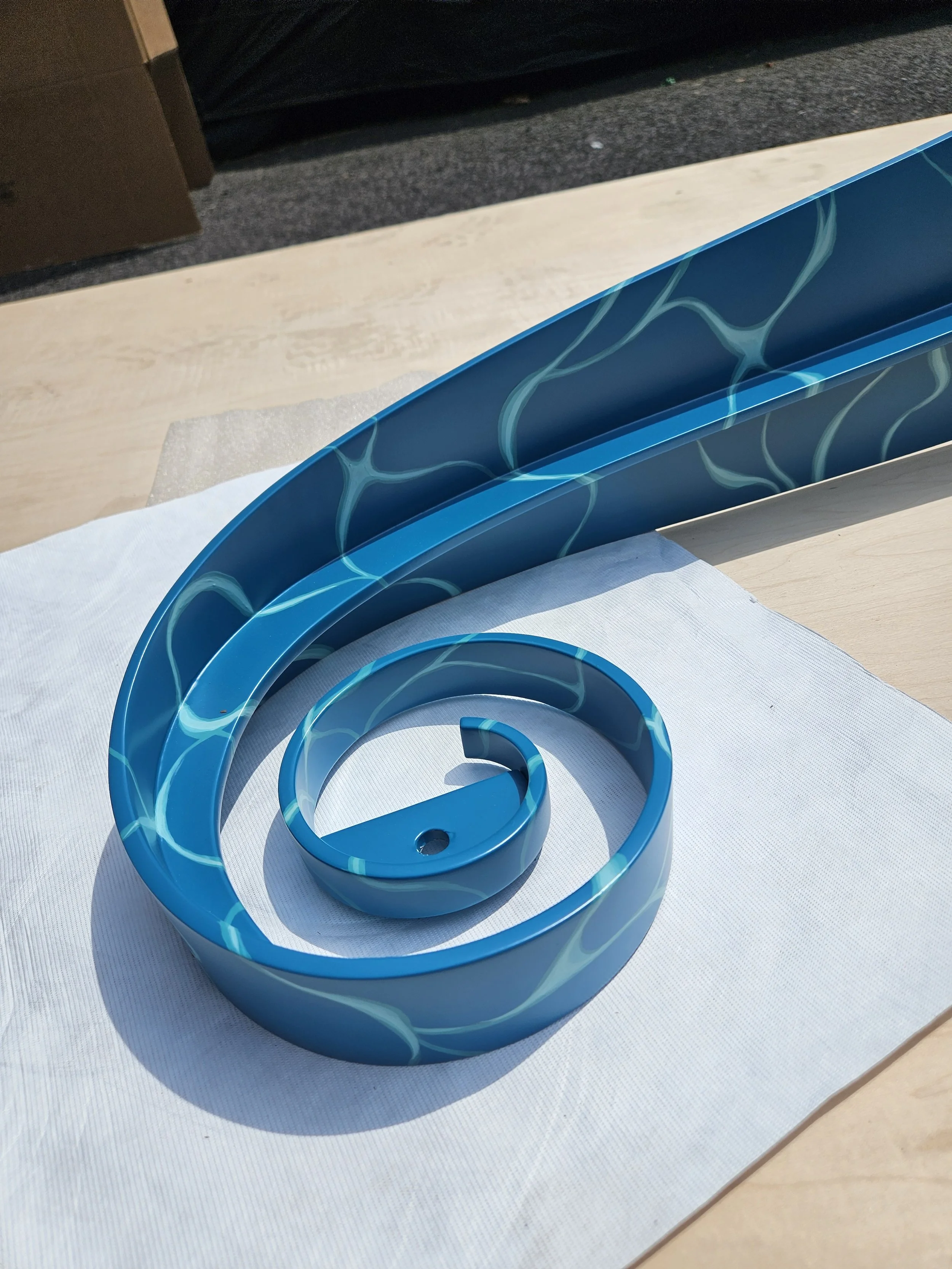 A blue, spiral-shaped plastic sign with water-like patterns, resting on a white cloth on a wooden surface.