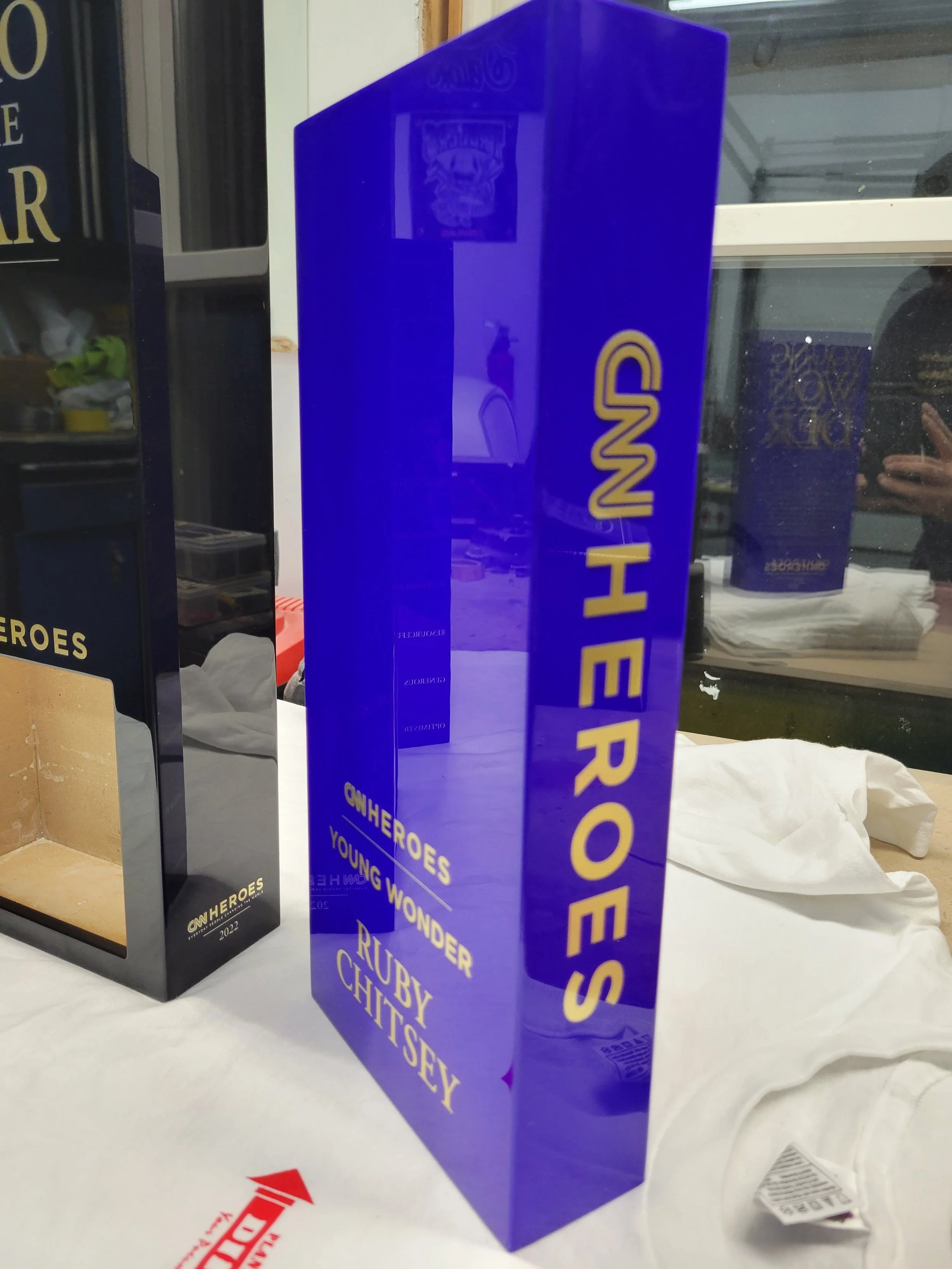 Blue rectangular block with gold text reading 'SHEROES' and additional smaller text 'HEROES YOUNG WONDER RUBY CHITSEY' on the front and side.