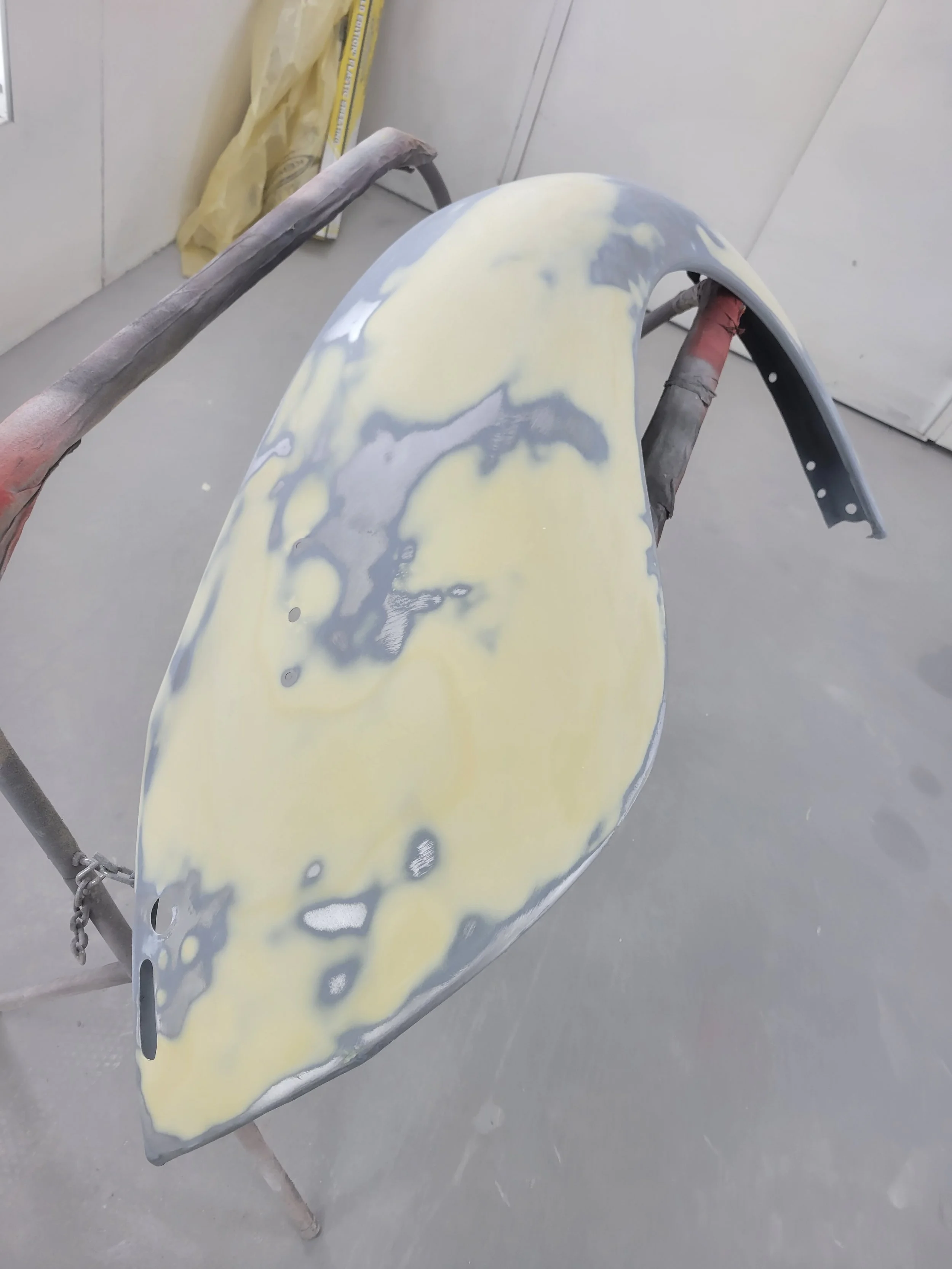 Car bumper being prepared for painting, with primer and sanding marks visible.