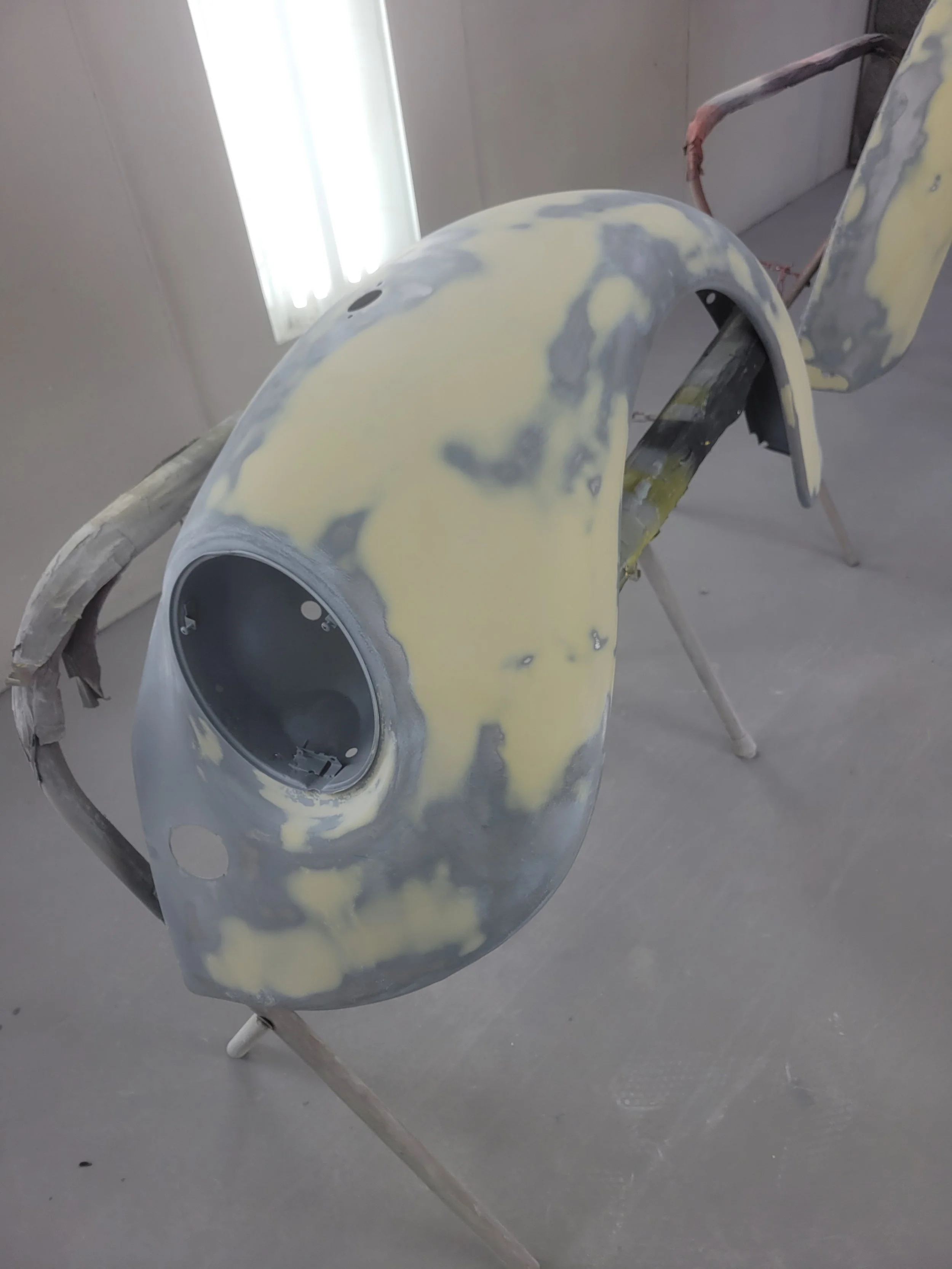 A partially assembled motorcycle fairing with a hole for the headlight, attached to a stand in a workshop.