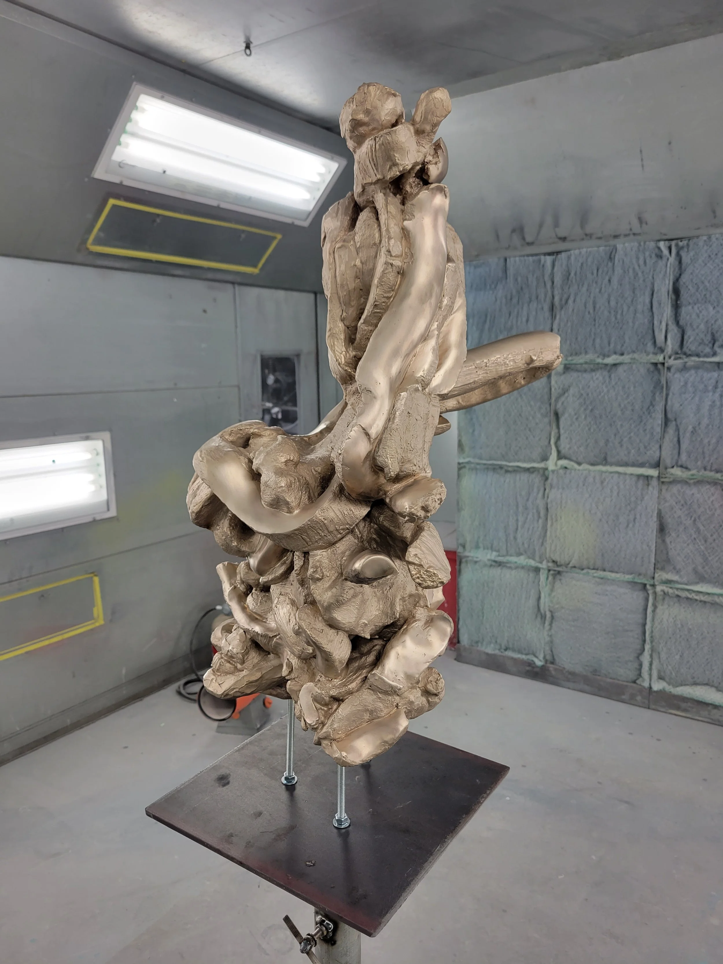 A sculpture made of clay or similar material on a small platform in a workshop or studio with fluorescent lights and soundproofing foam walls.