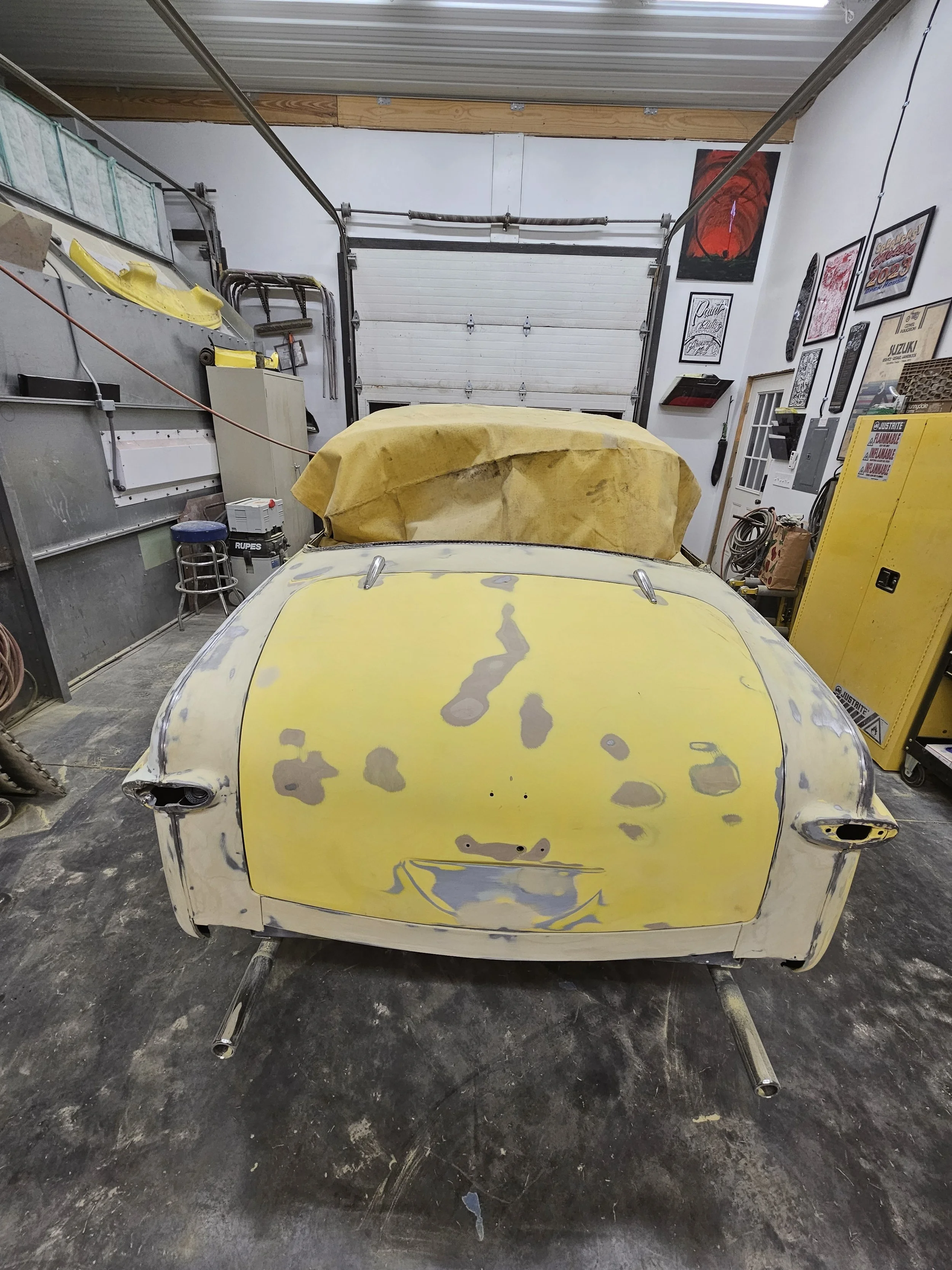 A yellow car body with paint sanding and primer marks inside a garage workshop.