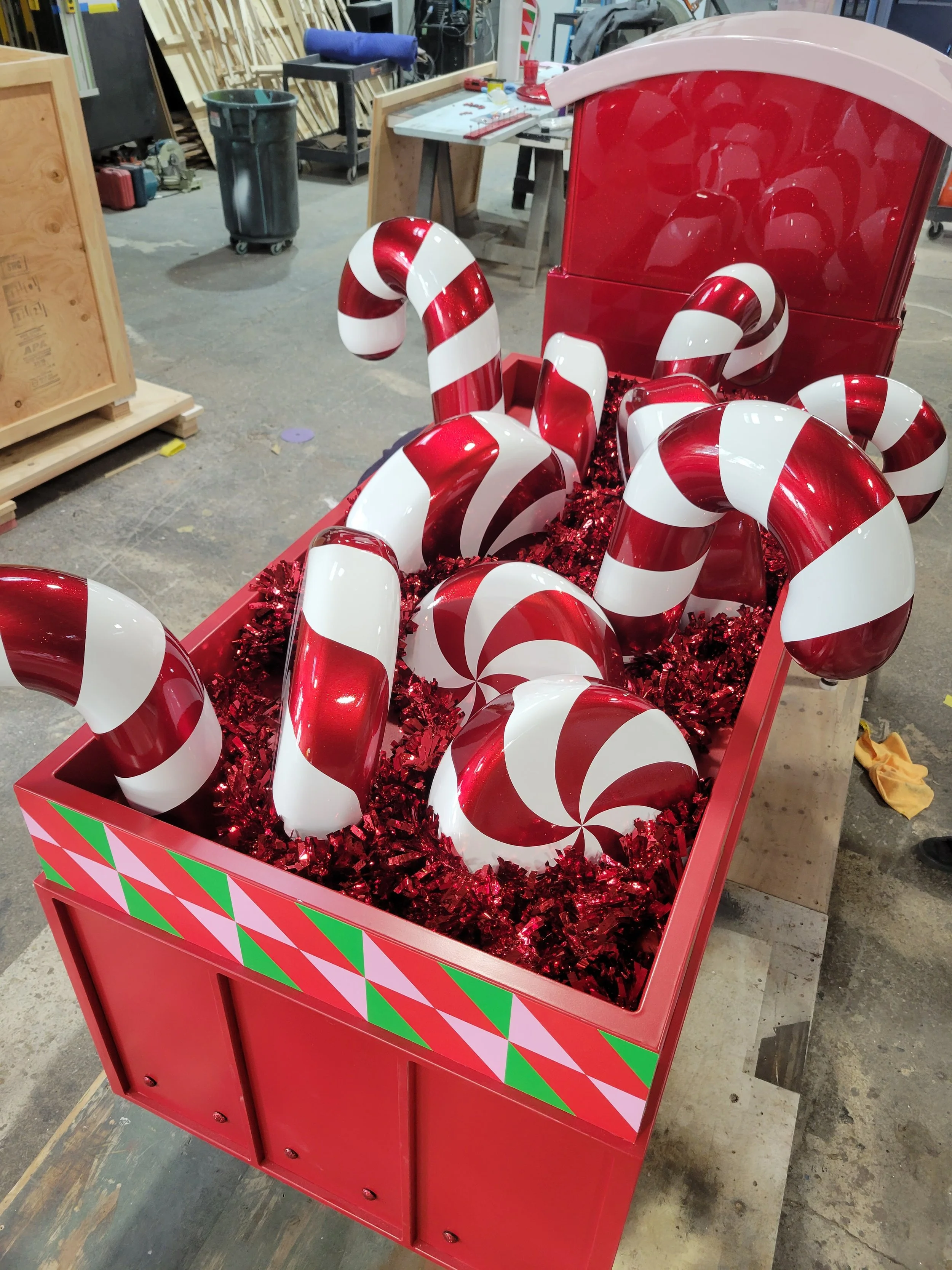 A red Christmas-themed display box filled with red and white swirled candy canes and peppermint candies, decorated with red tinsel.