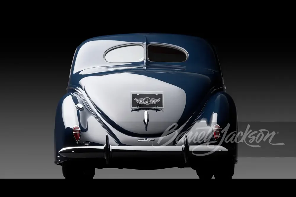 Back view of a vintage luxury car with a sleek, dark blue and silver exterior, rear window, and tail lights.