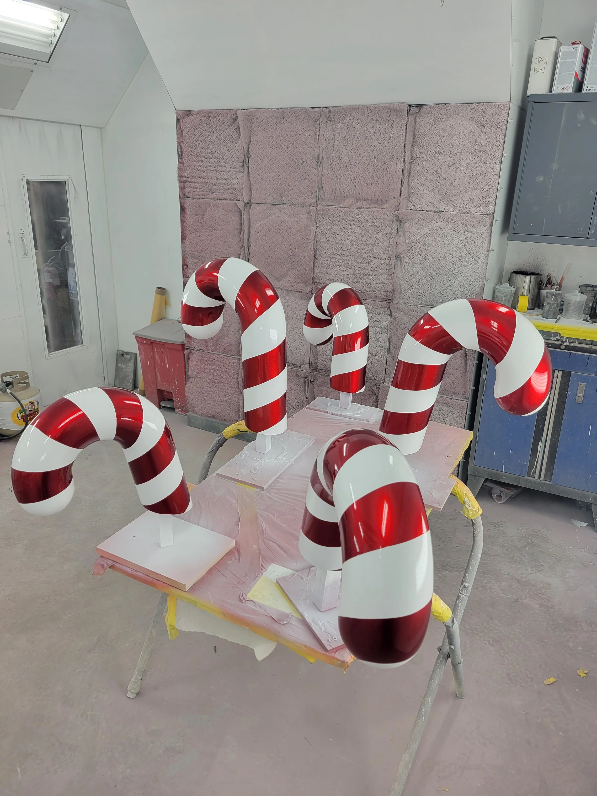 Five candy cane decorations with red and white stripes on a worktable in a workshop.