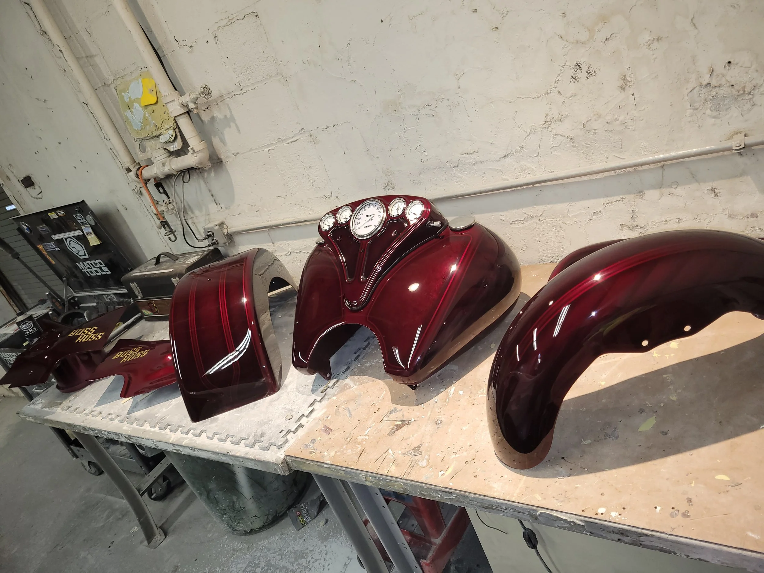 Disassembled motorcycle parts including a fuel tank, headlight, and fenders on a workbench in a garage.