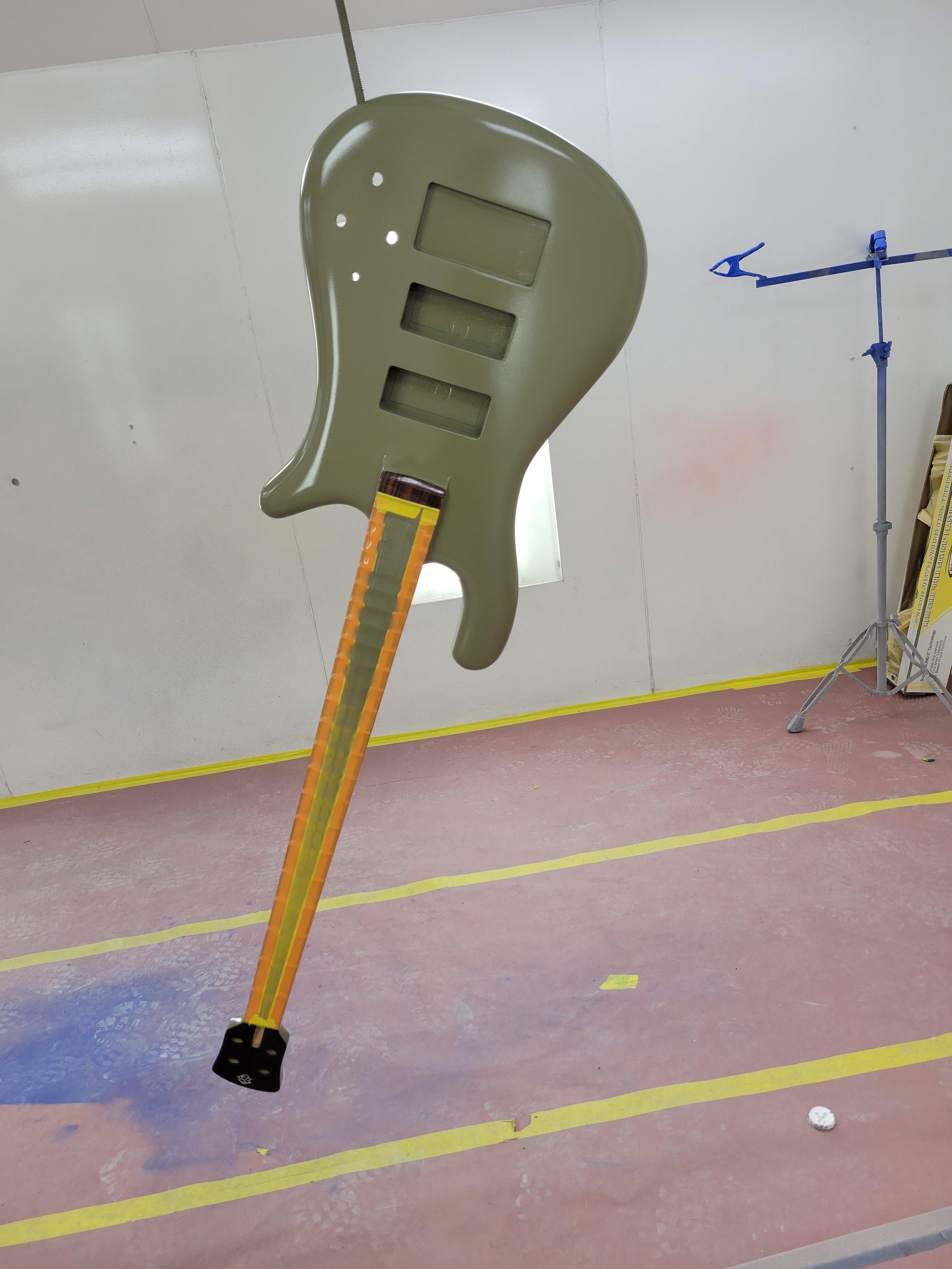 An inflatable guitar with a beige body and an orange neck floating in a room with pink flooring and white walls.