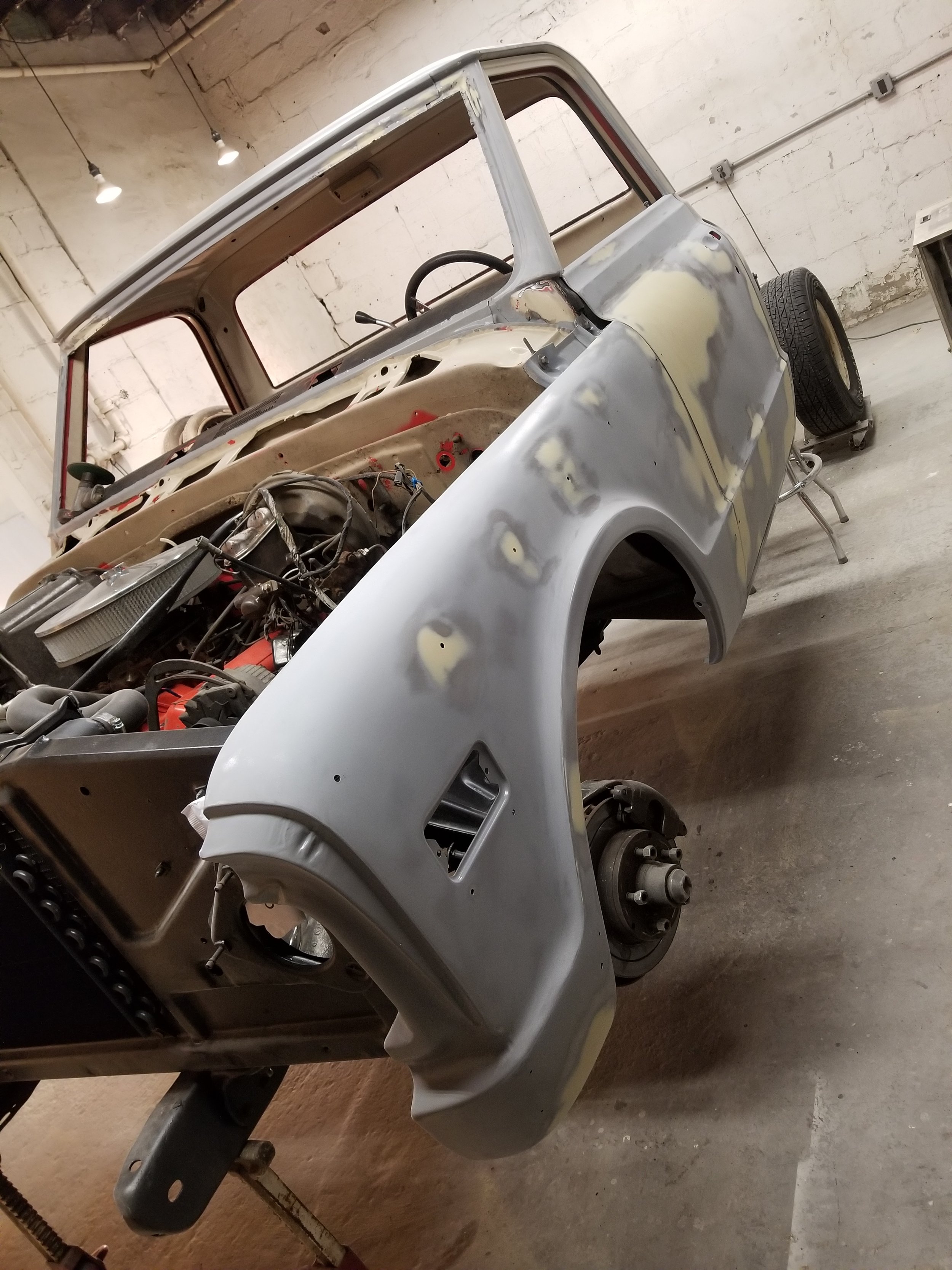 A classic car undergoing restoration in a workshop, with its body partially painted, exposed engine, and wheels removed.