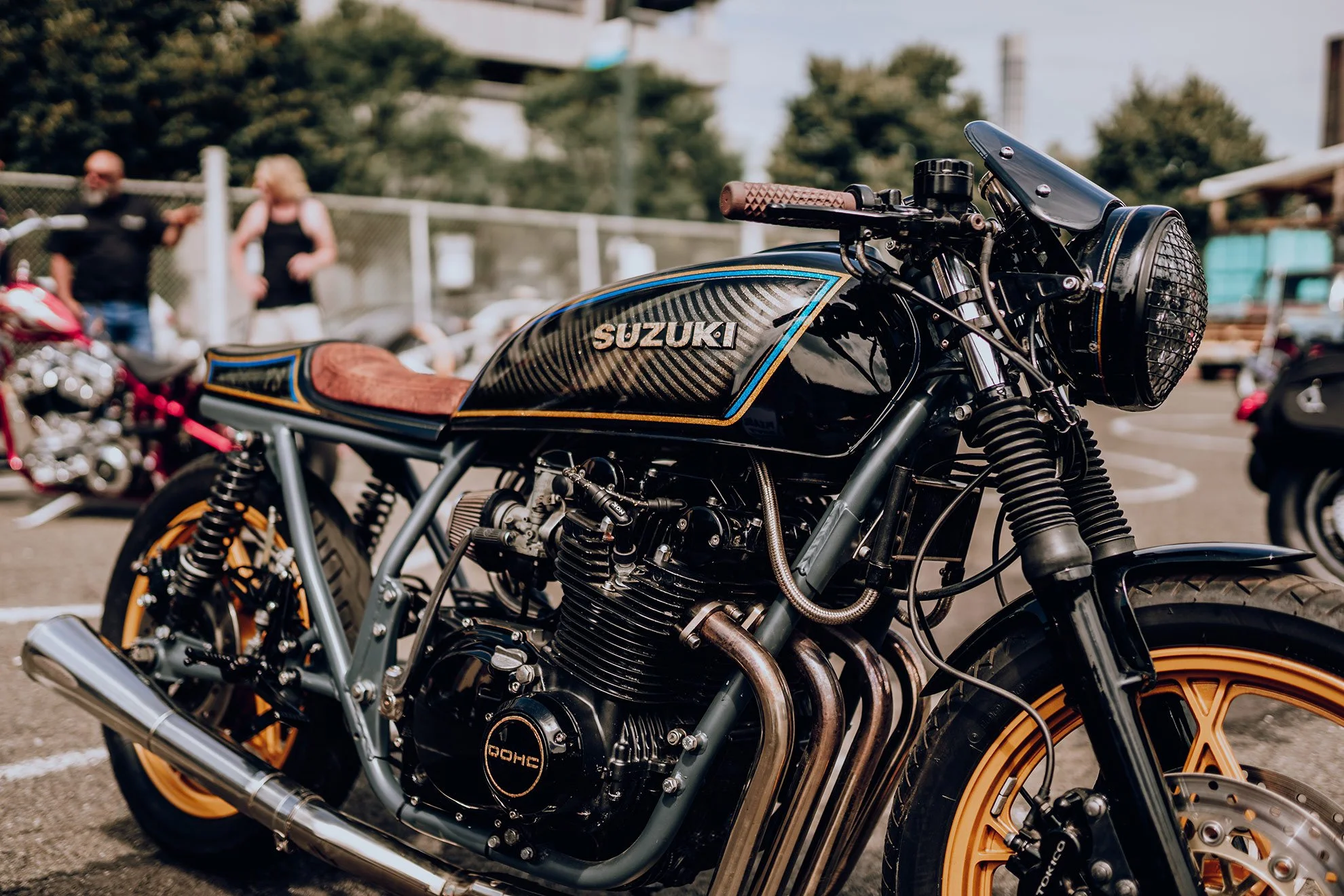 Close-up of a custom black and gold Suzuki motorcycle with wooden accents, parked outdoors at a motorcycle event.