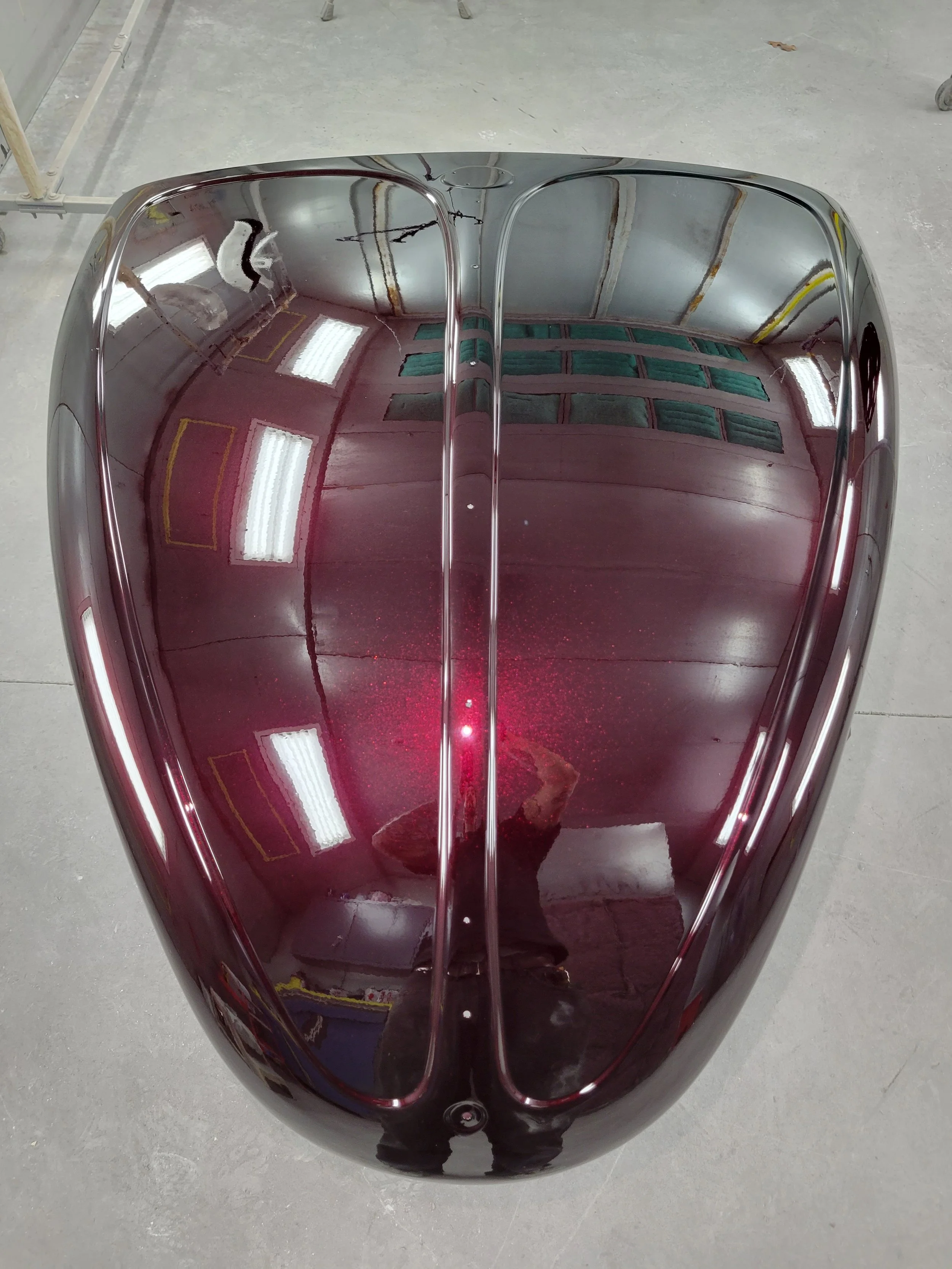 A shiny, dark red, metallic car hood with a mirror-like finish, reflecting the ceiling lights and surrounding area.