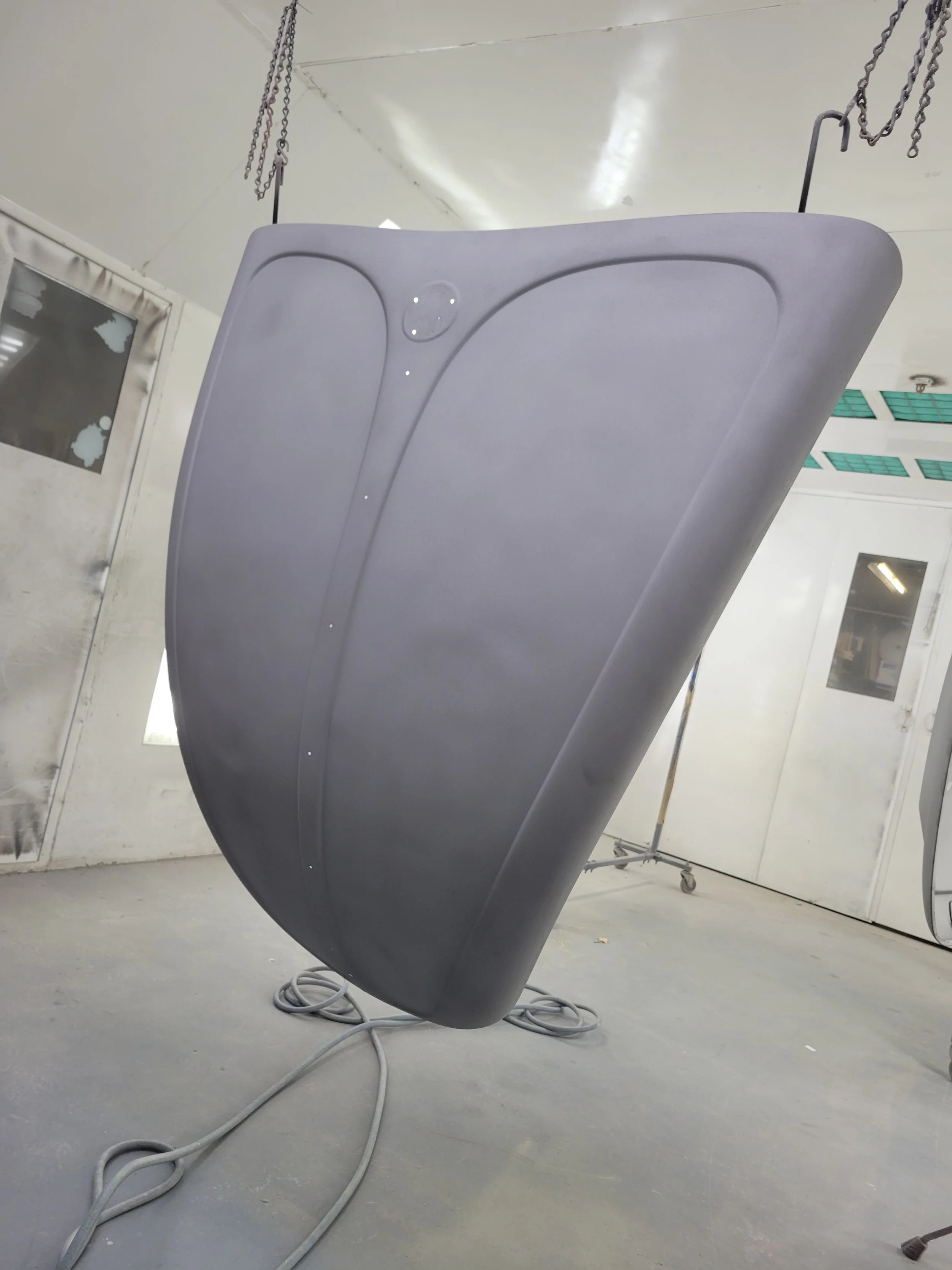 Front of a matte black car hood hanging in a paint booth.