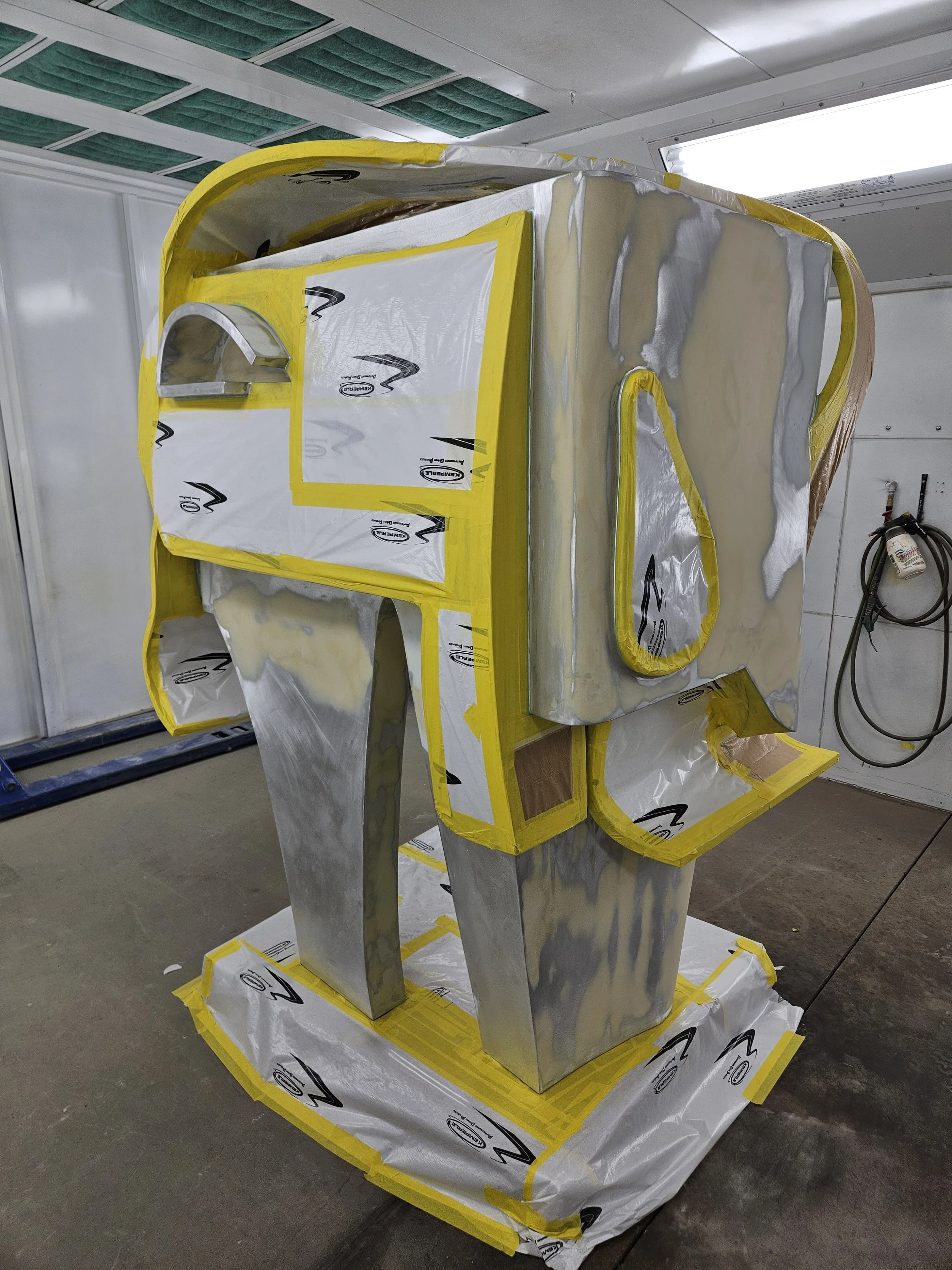 A partially assembled vehicle door with yellow masking tape, foam, and metal panels in a workshop setting.