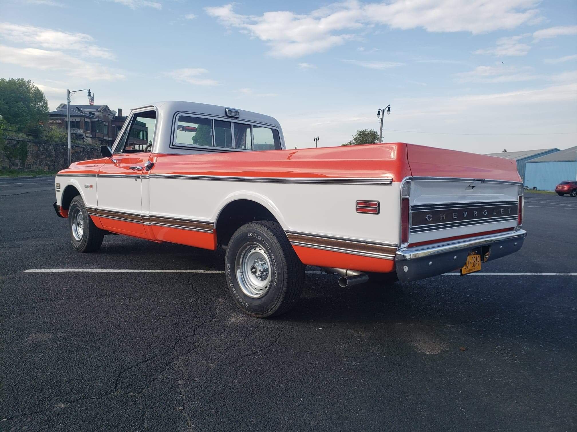 A vintage Chevrolet pickup truck with a white body and orange accents parked on a paved lot at sunset.