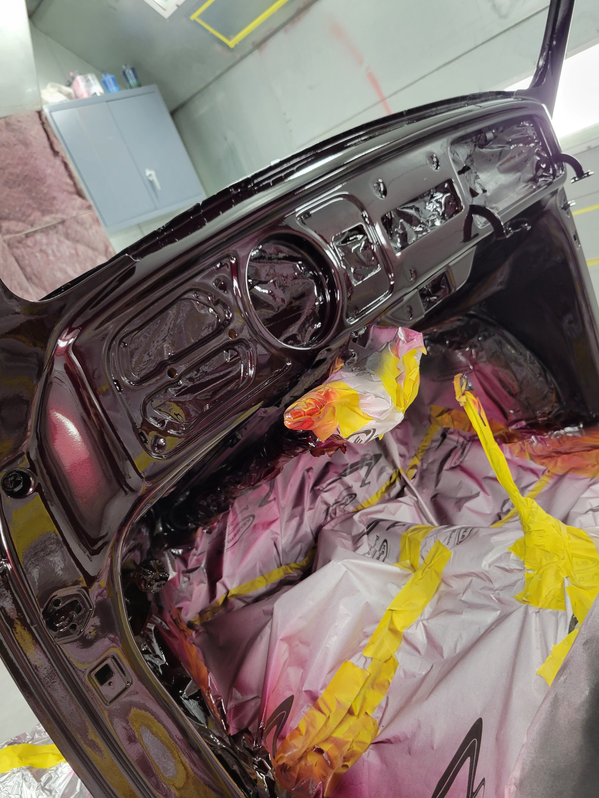Car dashboard and interior parts being painted or restored, covered with masking paper and tape.