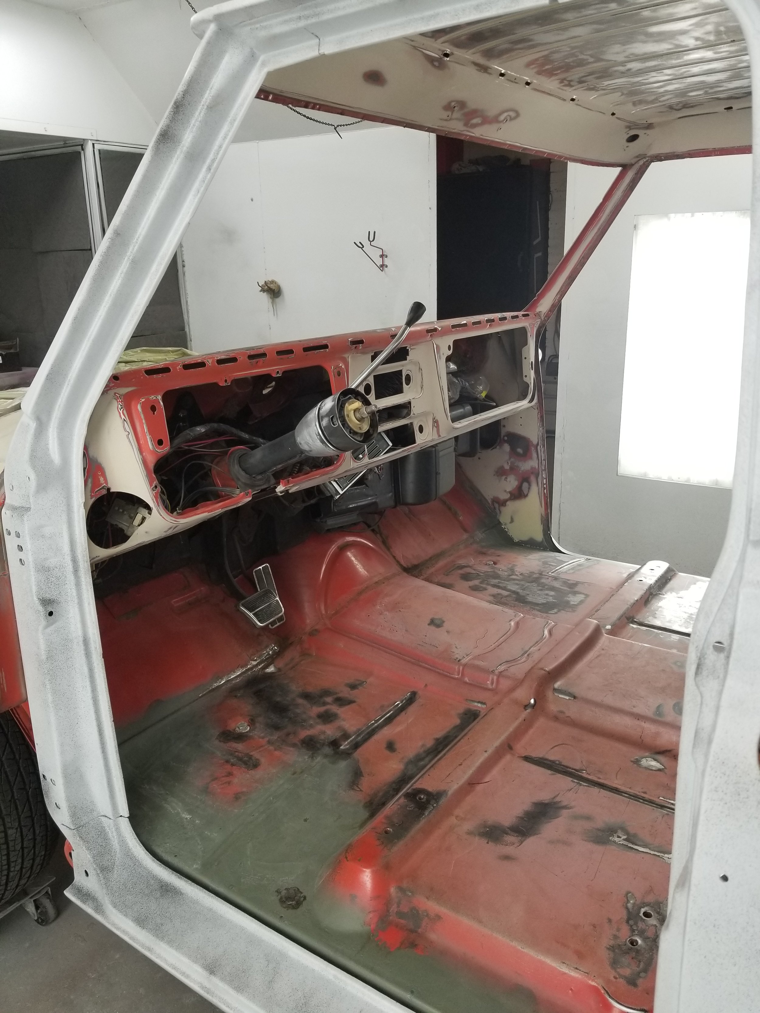 Interior of a vintage car in the process of restoration, showing the dashboard, steering column, and floor with no seats installed.