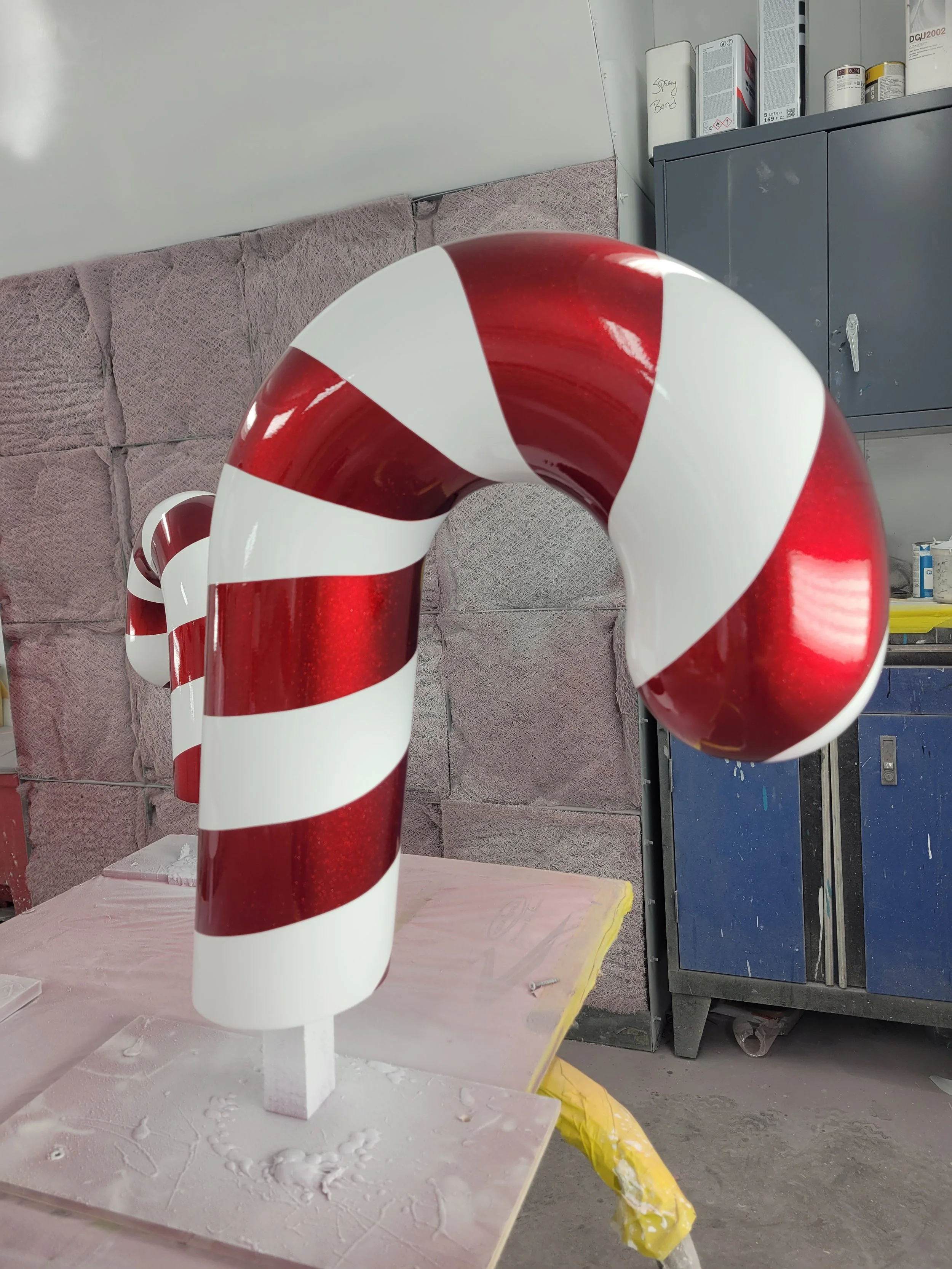 A decorative candy cane sculpture with red and white stripes, placed on a stand in a workshop.