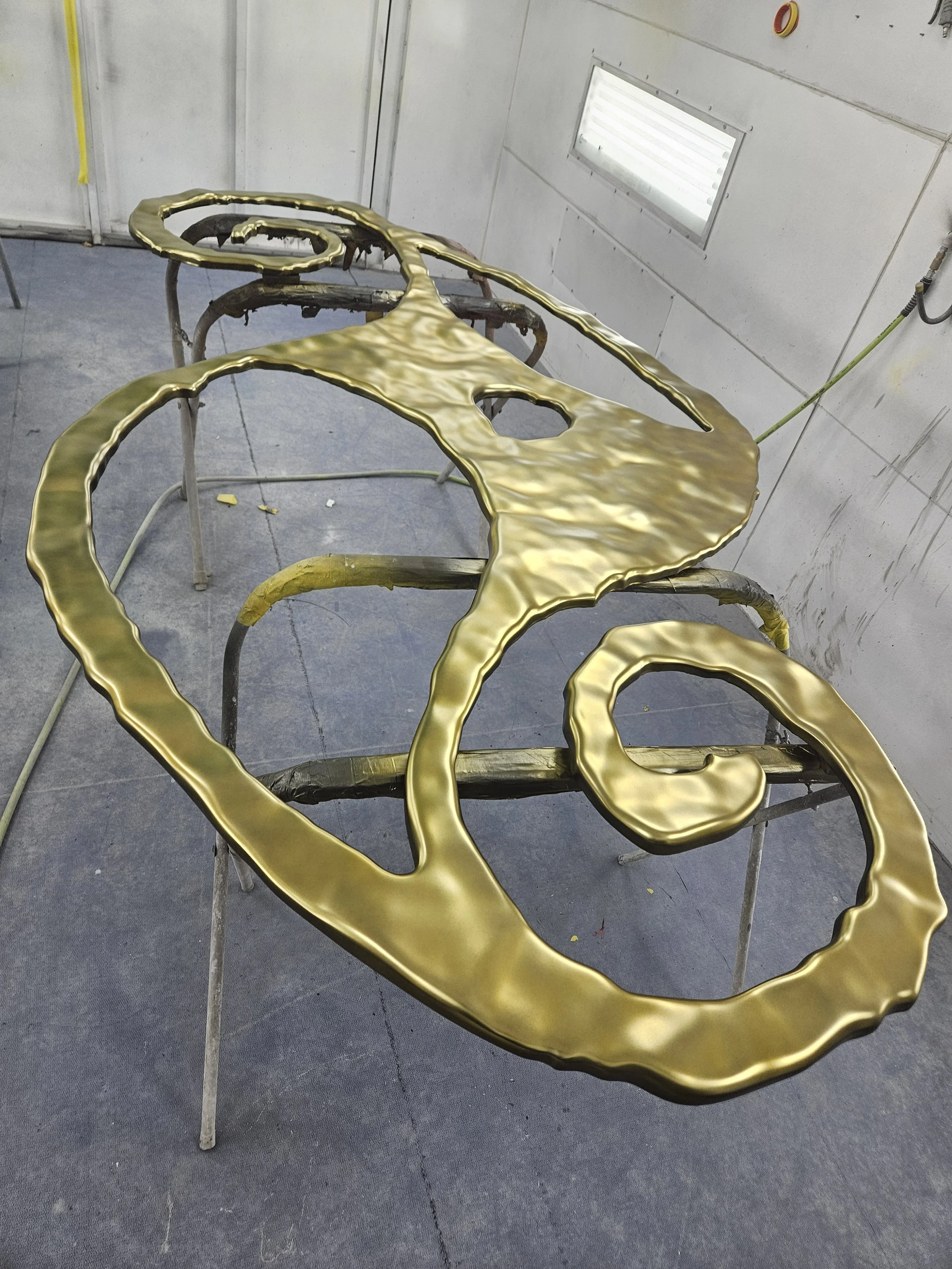 Metal artwork in progress, with gold-colored sections on a worktable in a workshop.