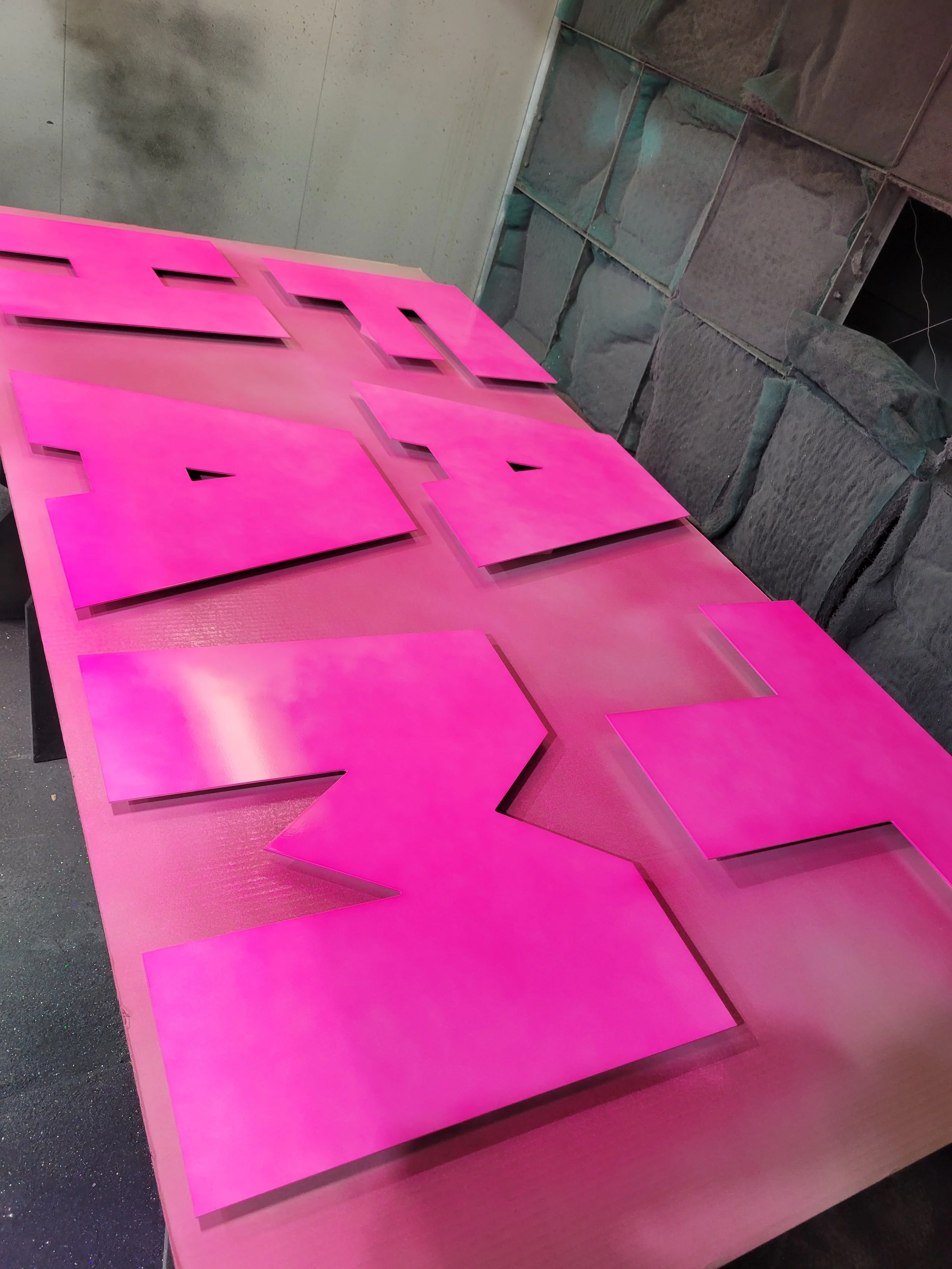 Pink signs with cutout letters on a pink table in a workshop setting.