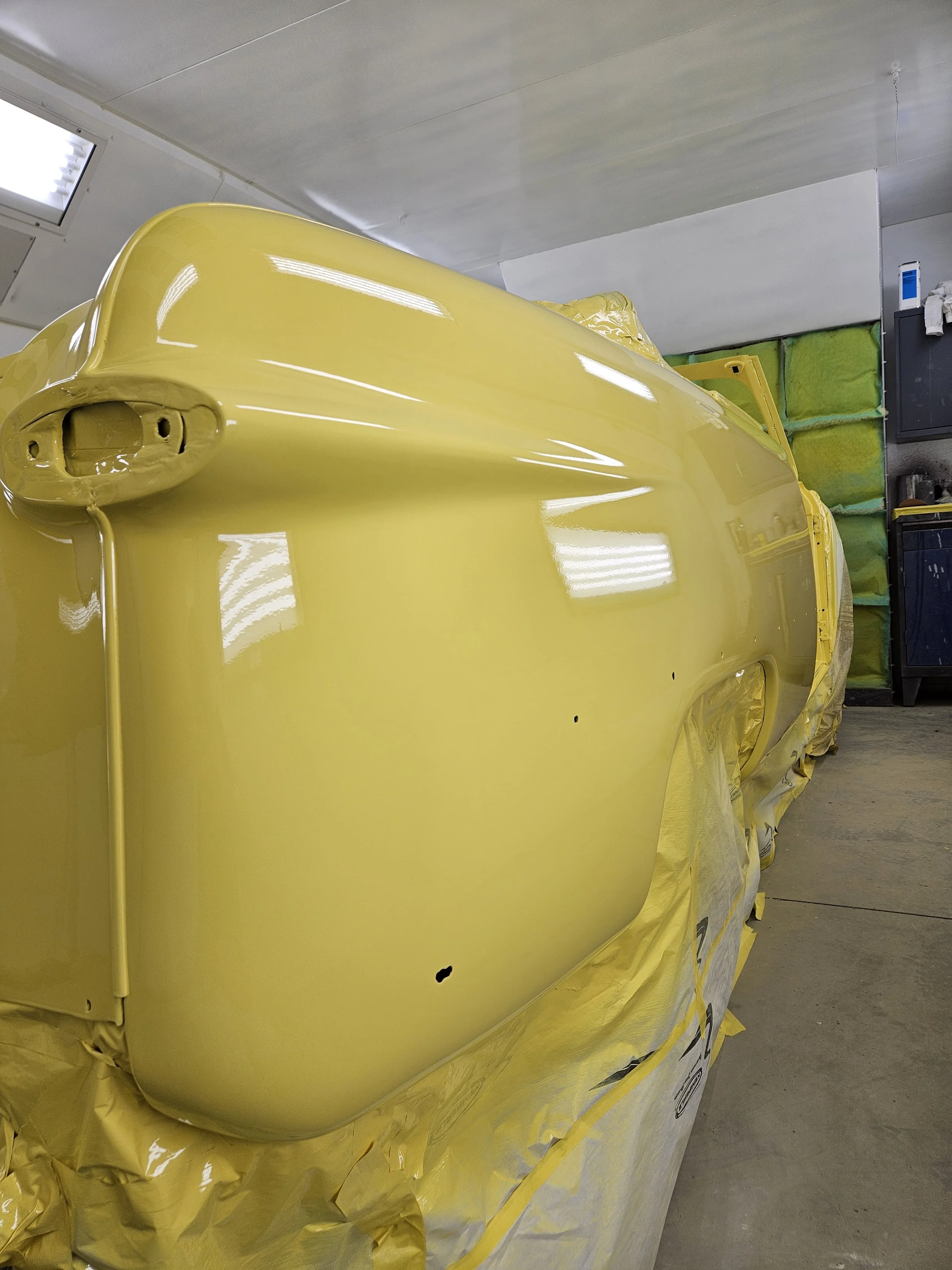 A car painted in bright yellow in a paint booth, with masking paper covering its lower part.