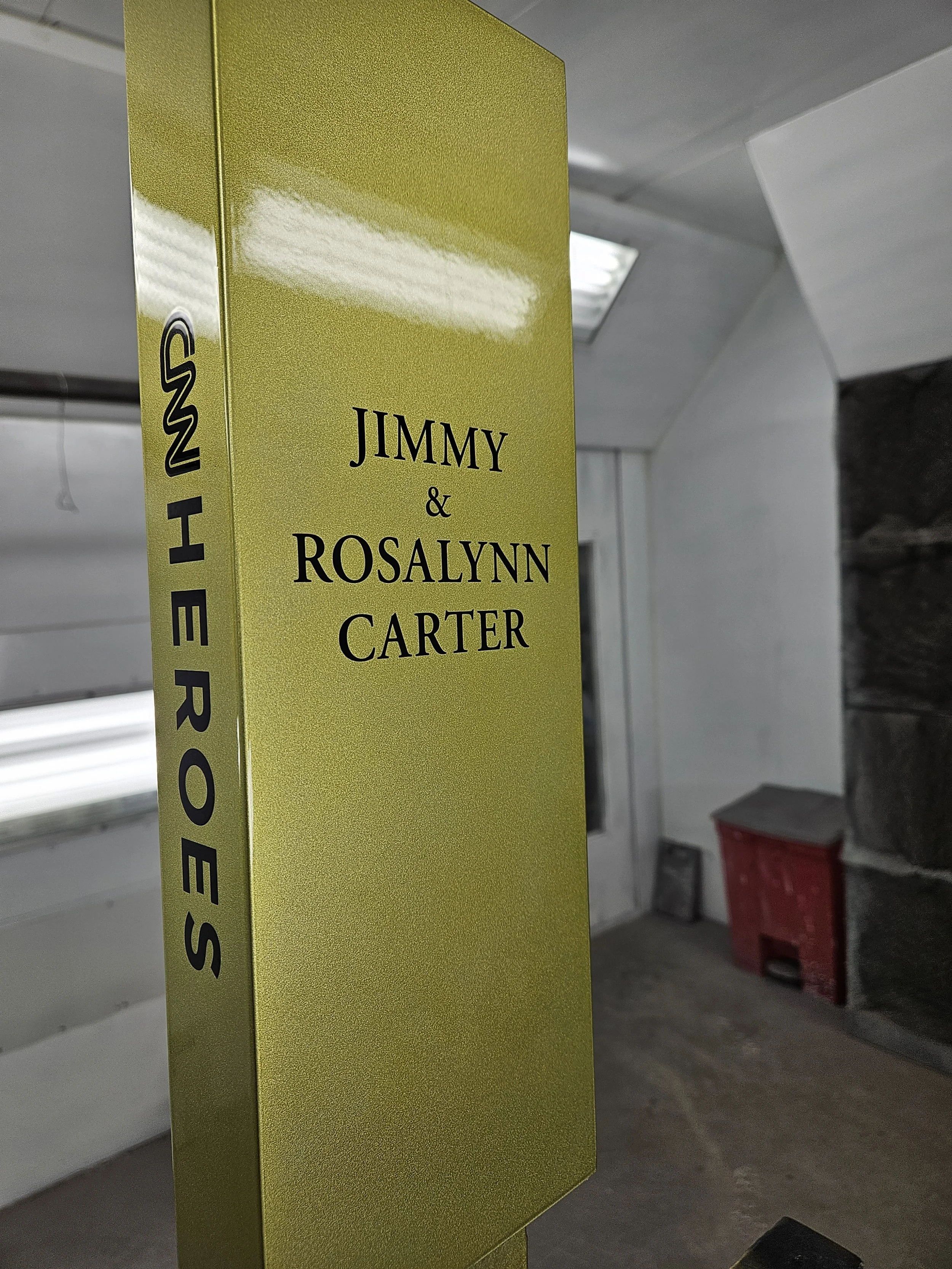 A yellow standee displaying the names Jimmy and Rosalynn Carter in black text, with the side reading 'We are Heroes'.