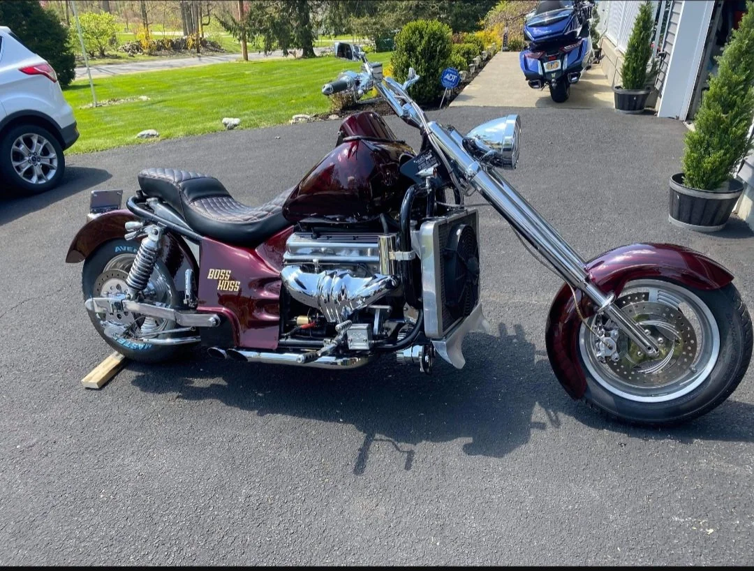 A custom motorcycle showing the frame and large chrome front fork, parked on a driveway 