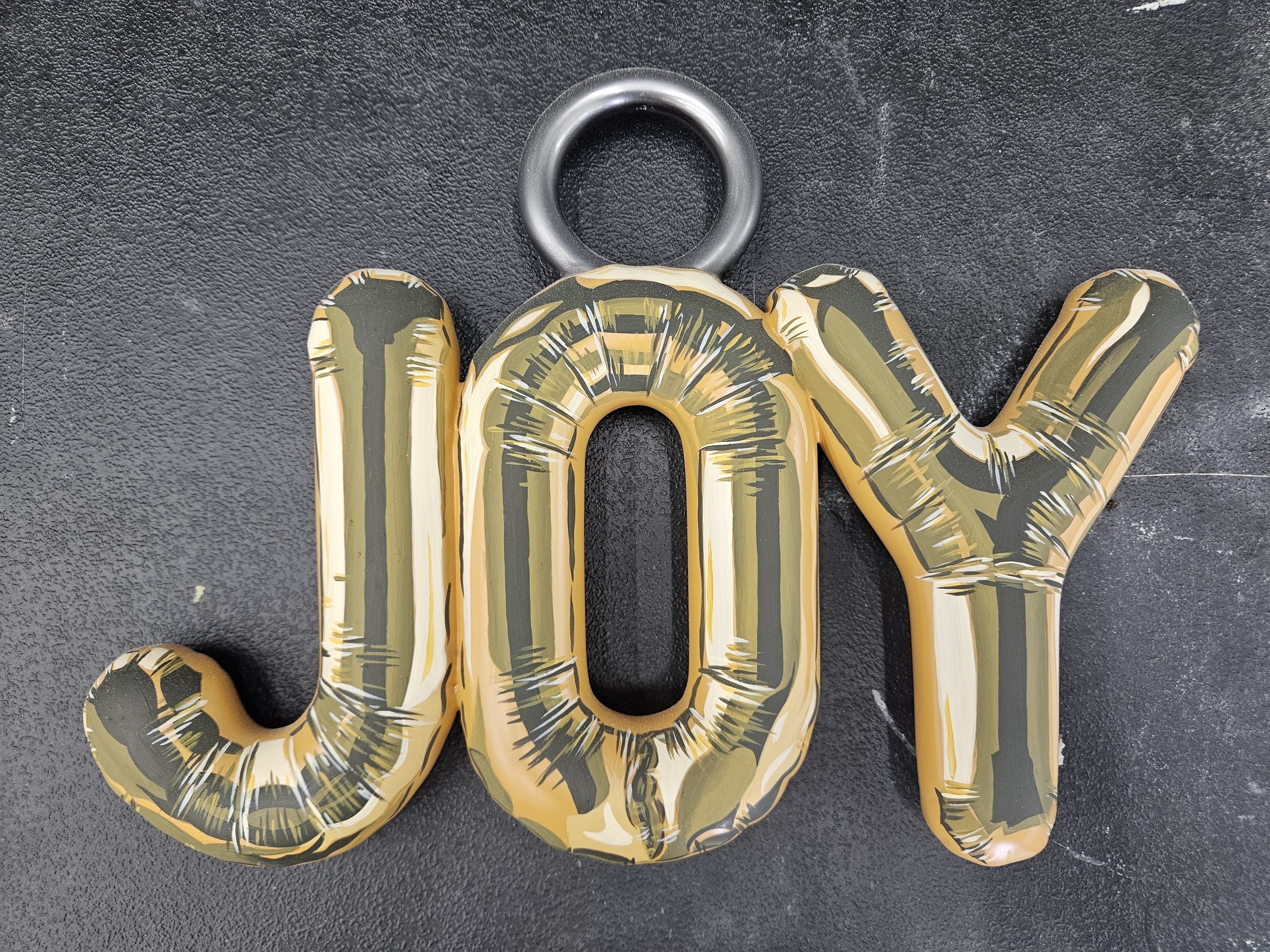 Gold and black balloon spelling out 'JOY' on a black surface.