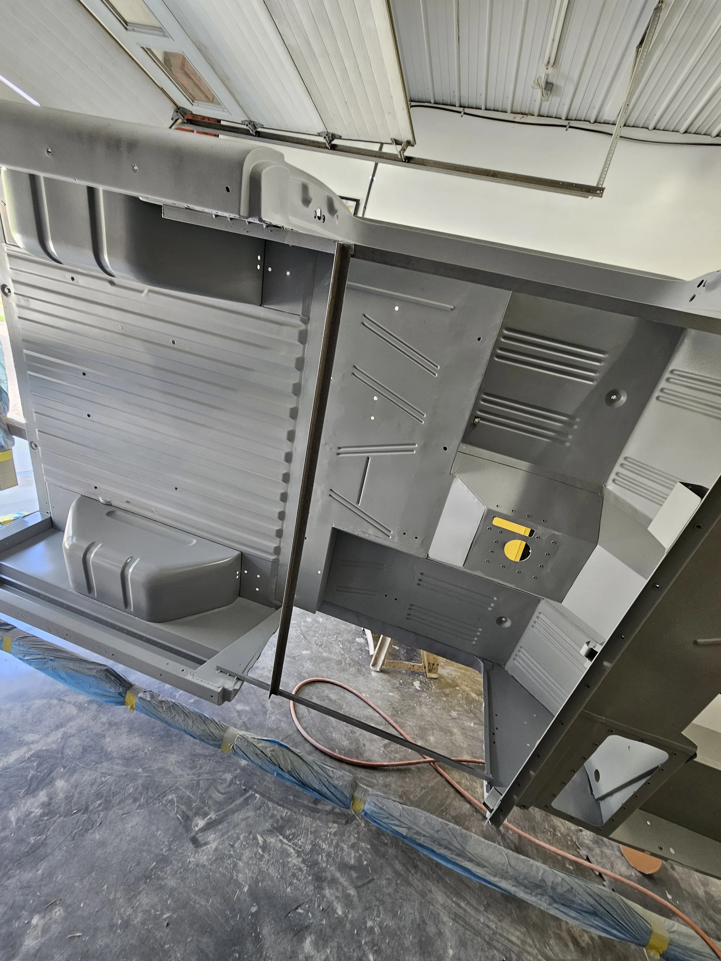 An industrial or mechanical structure made of gray metal, with ribbed and flat surfaces, situated indoors. It appears to be part of a larger assembly or machine, with a yellow component and a black bar or support.