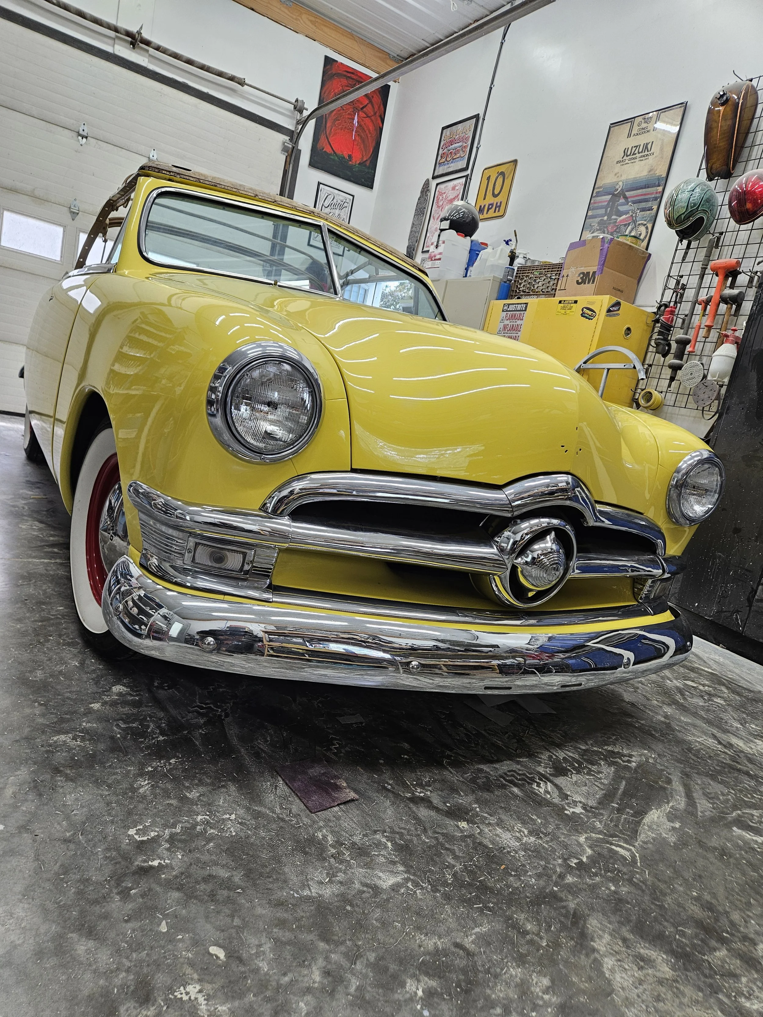 Yellow vintage car with chrome bumper and grill, whitewall tires, inside a garage or workshop.