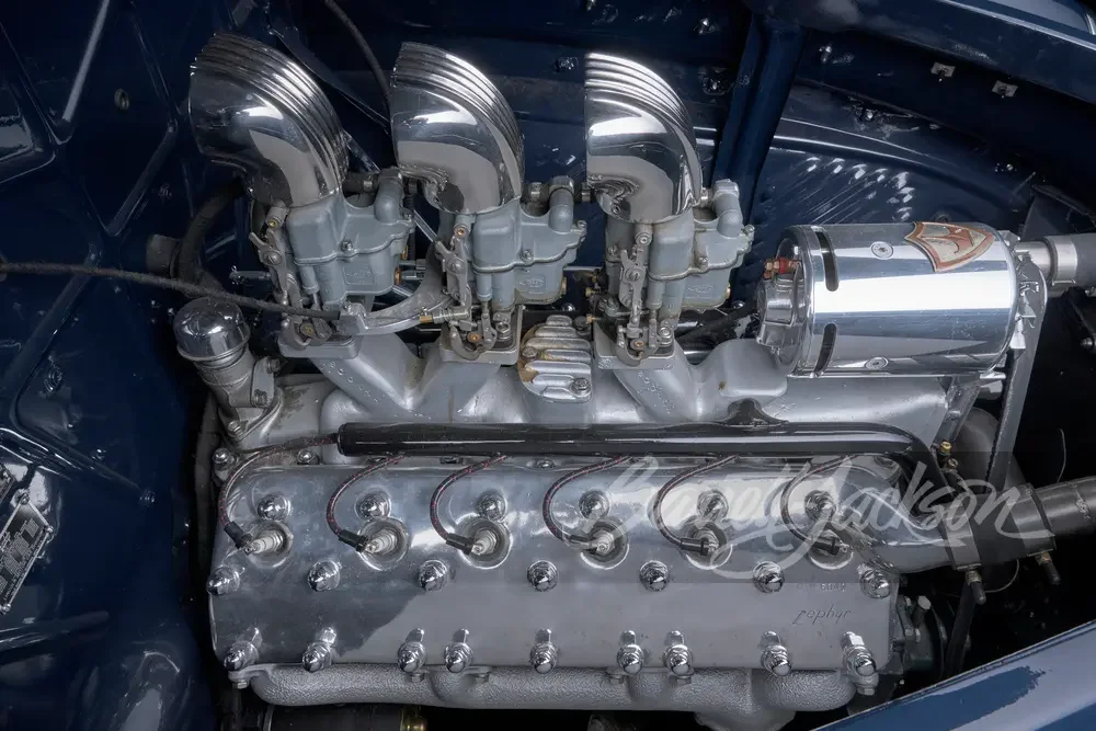 A vintage car engine showing four carburetors, spark plug wires, and a chrome air filter.