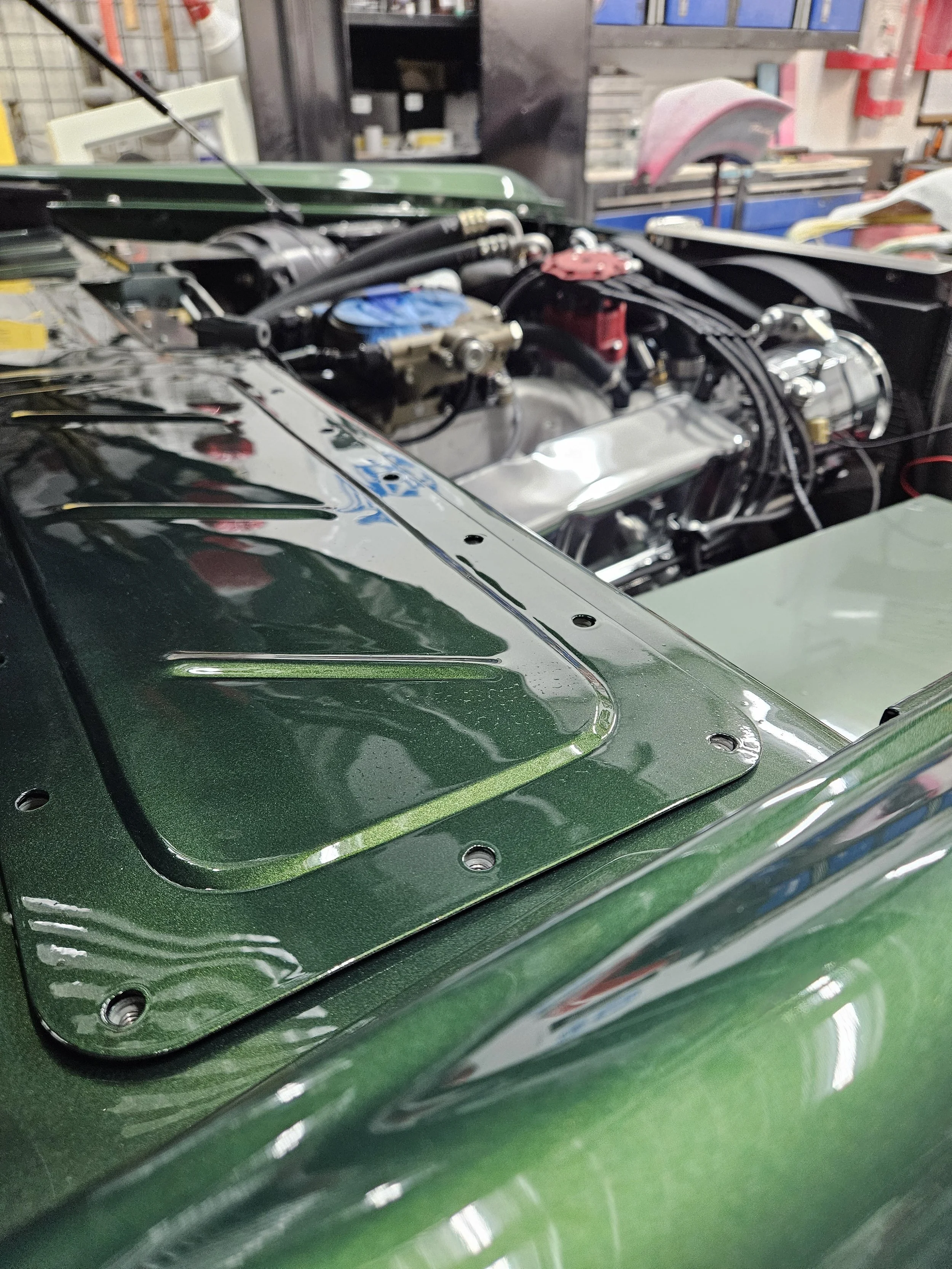 Close-up of a green car with an open hood, revealing parts of the engine in a workshop.