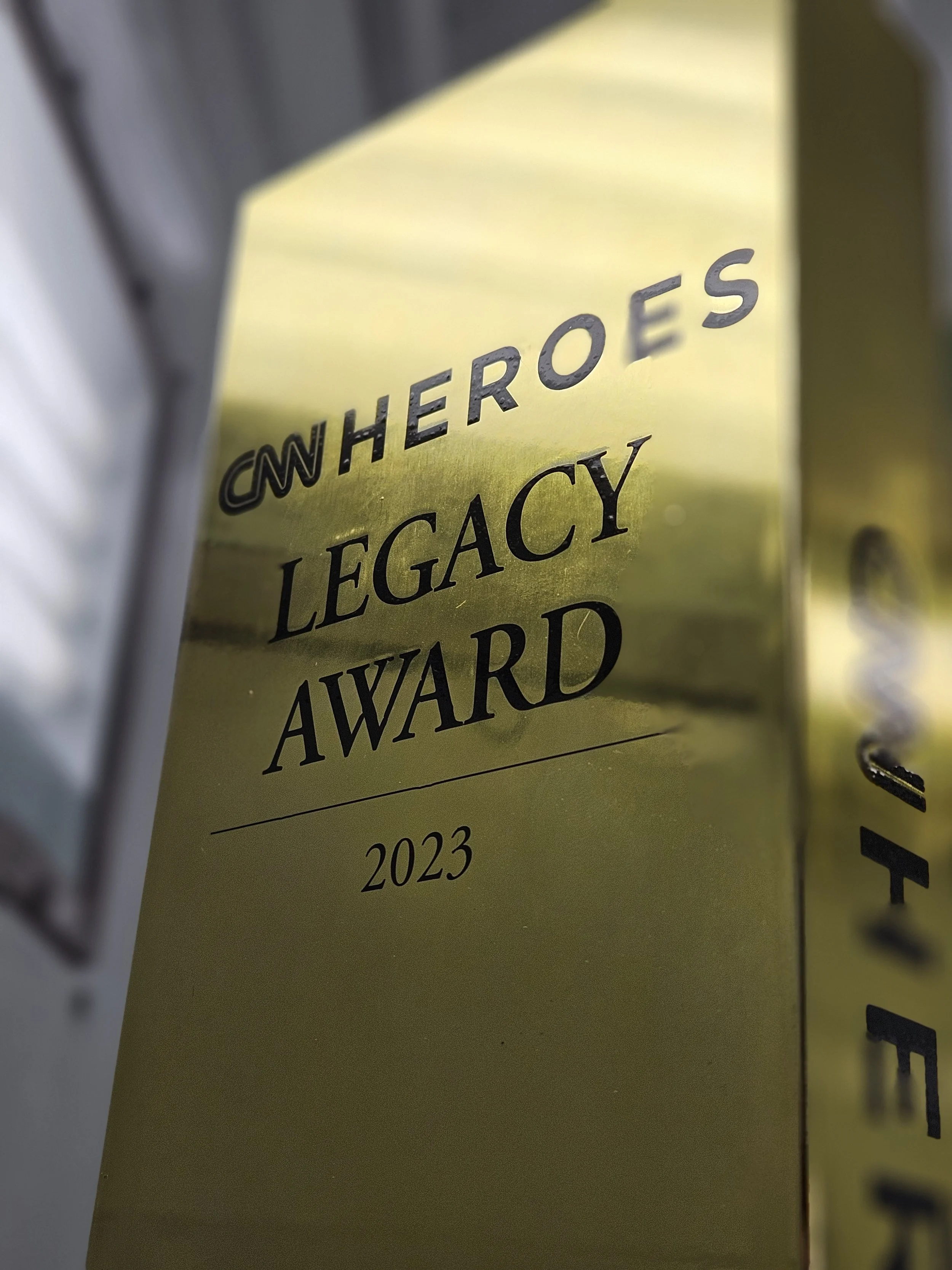 A close-up of a yellow award plaque that reads "CNN Heroes Legacy Award 2023".