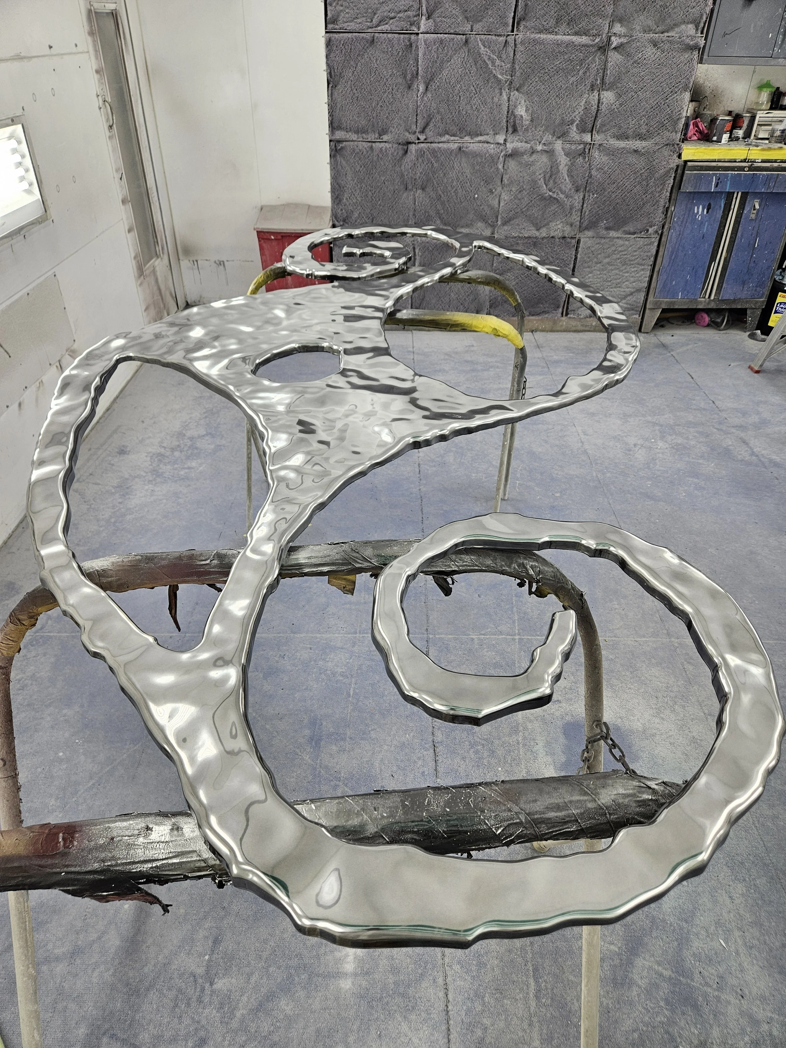 Metal sculpture of interconnected rings and shapes on a worktable in a workshop.