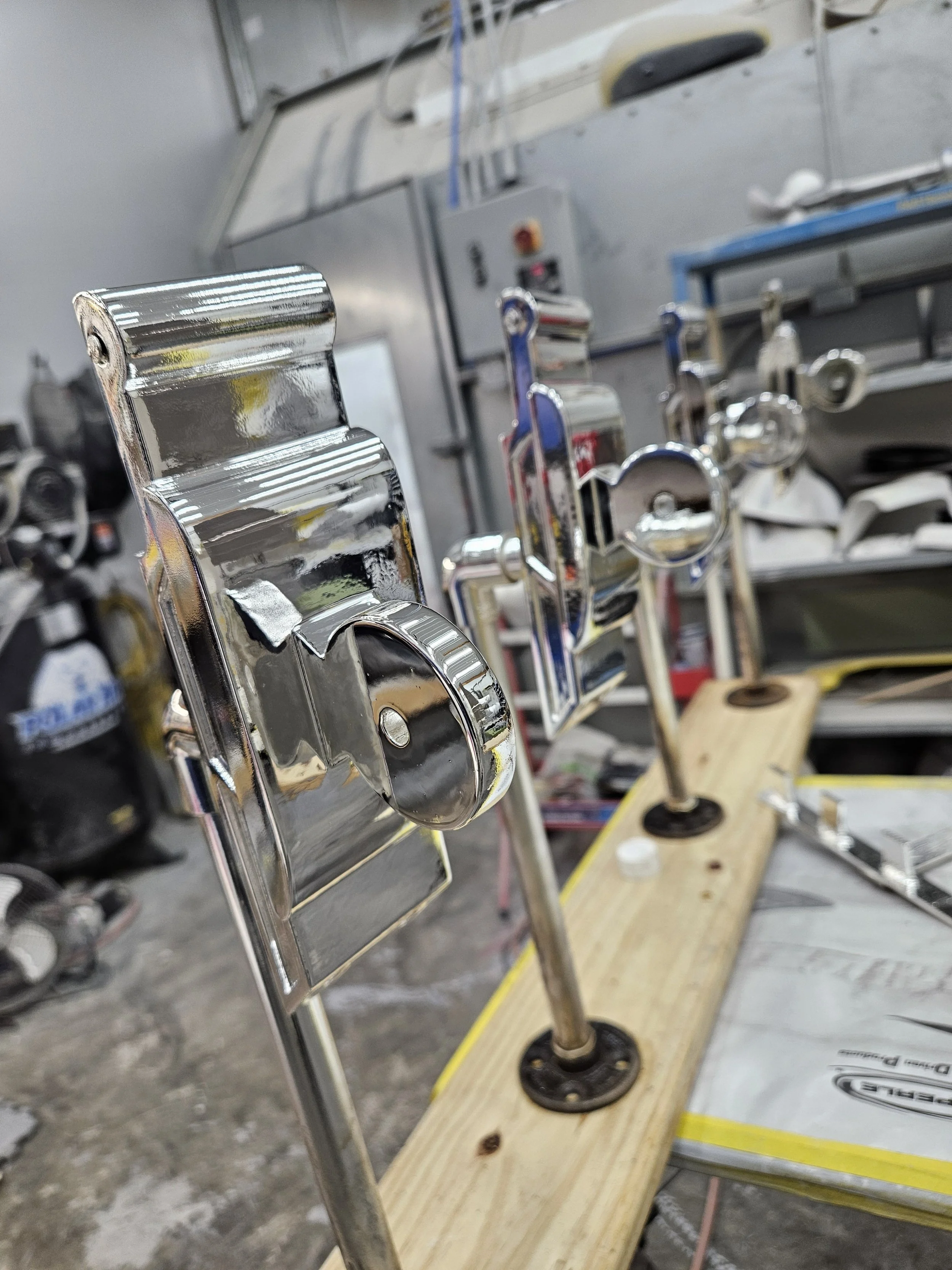 Close-up of shiny metallic car bumpers and metal parts on a workbench in a garage or workshop.