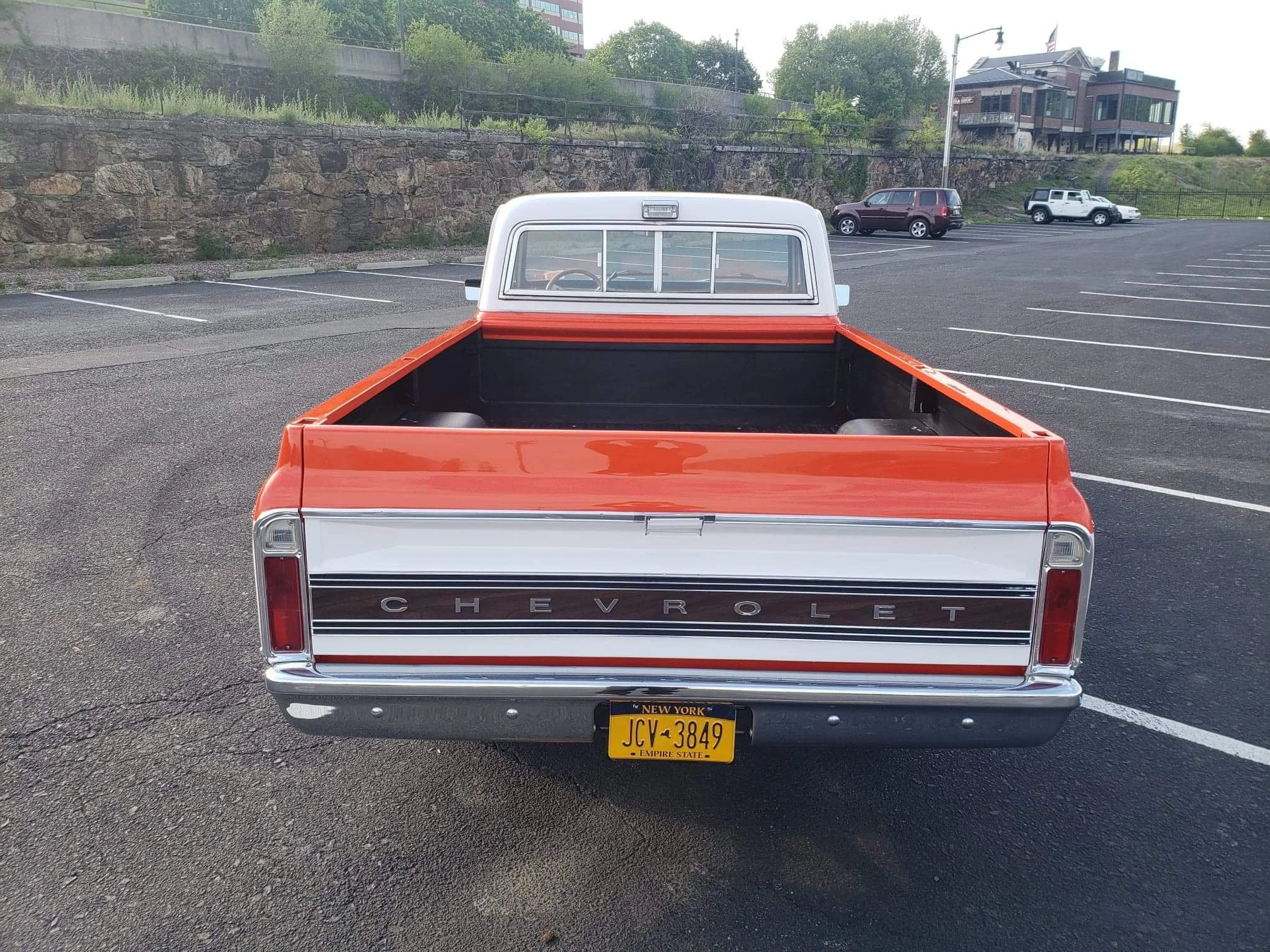 Rear view of a vintage Chevrolet pickup truck with orange and white body and a black bed, parked in an empty parking lot.