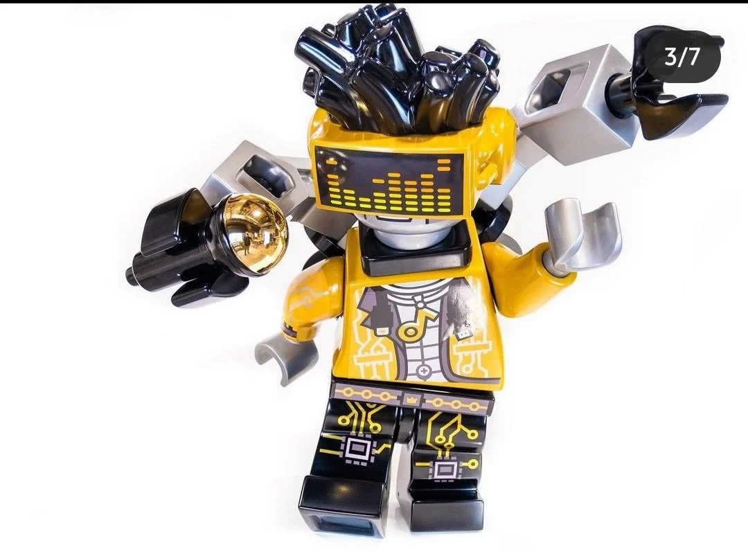 Lego robot figure with a yellow jacket, black and yellow legs, and a digital display face, holding a golden sphere and a silver cube.