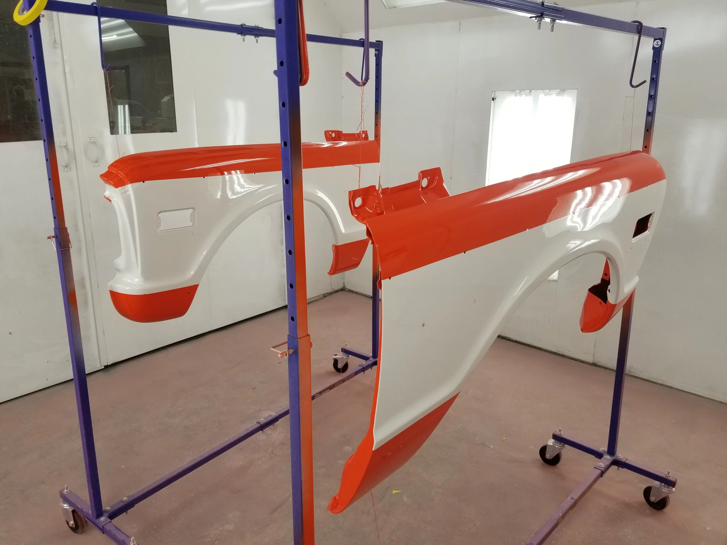 Auto body parts painted white and orange mounted on a metal stand in a workshop