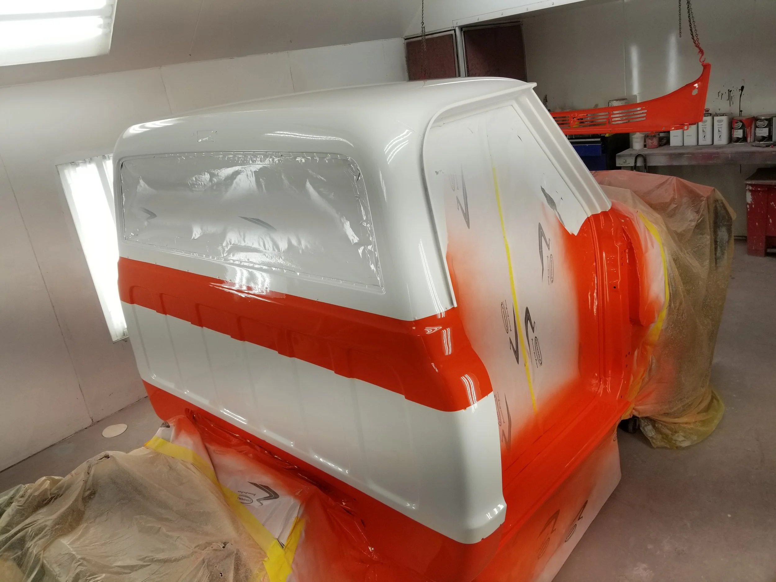 Vehicle cabin being painted with orange and white colors in a paint booth.