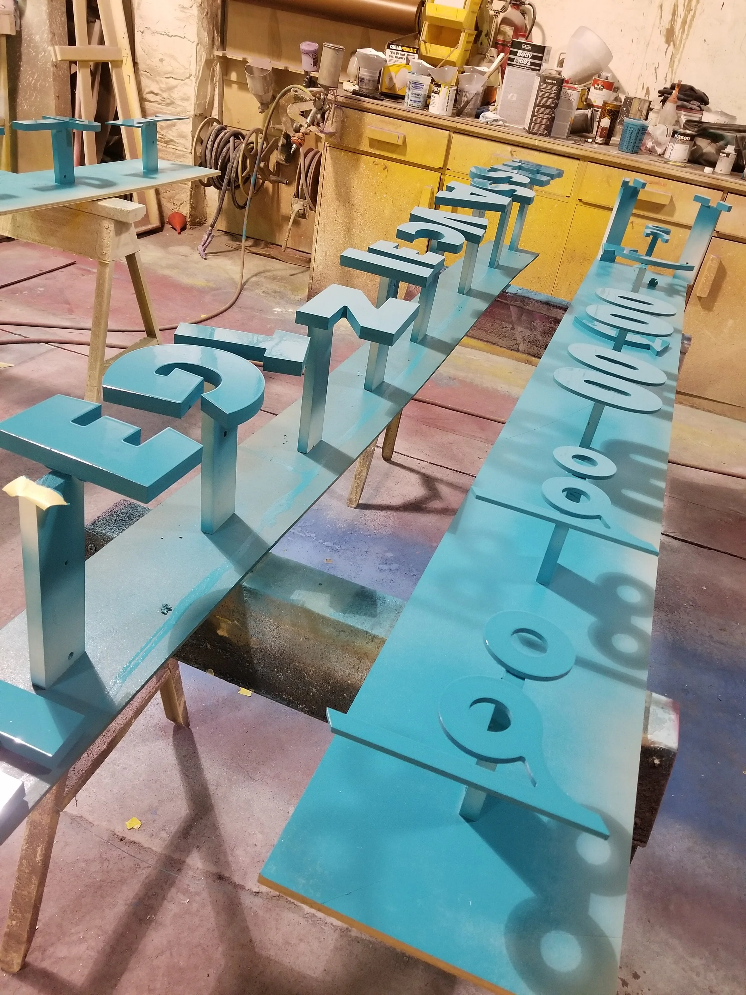 Blue 3D cutout numbers arranged on work tables in a workshop.