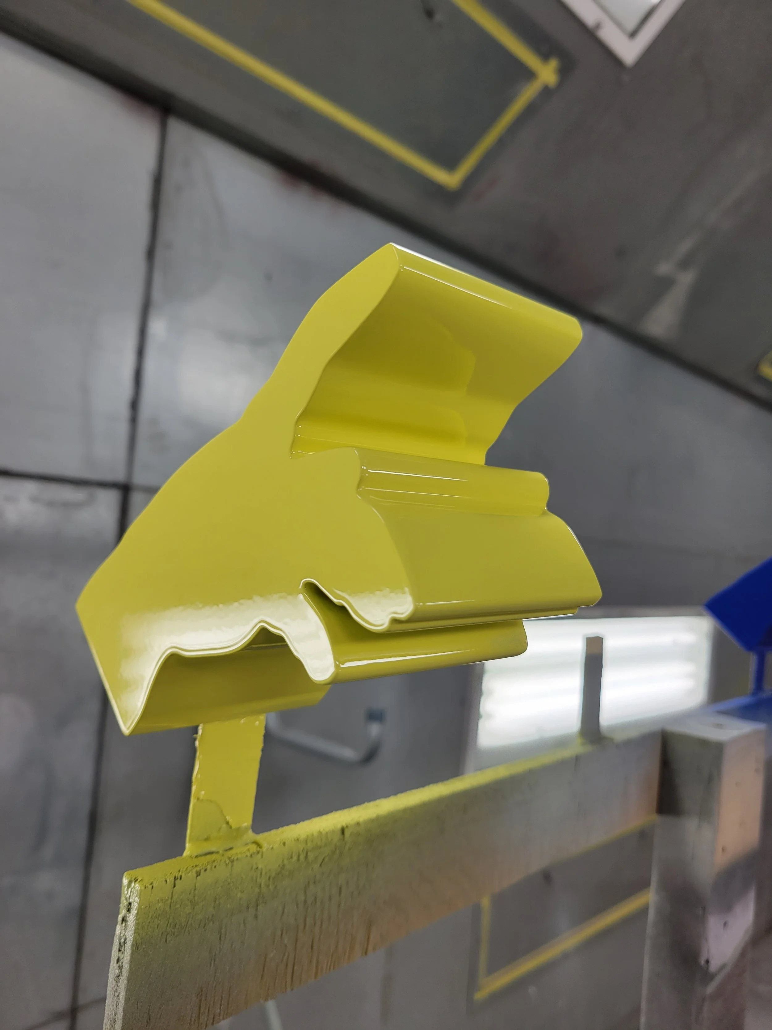 Close-up of a yellow metal object with a reflective surface, mounted on a wooden support in an industrial or workshop setting.